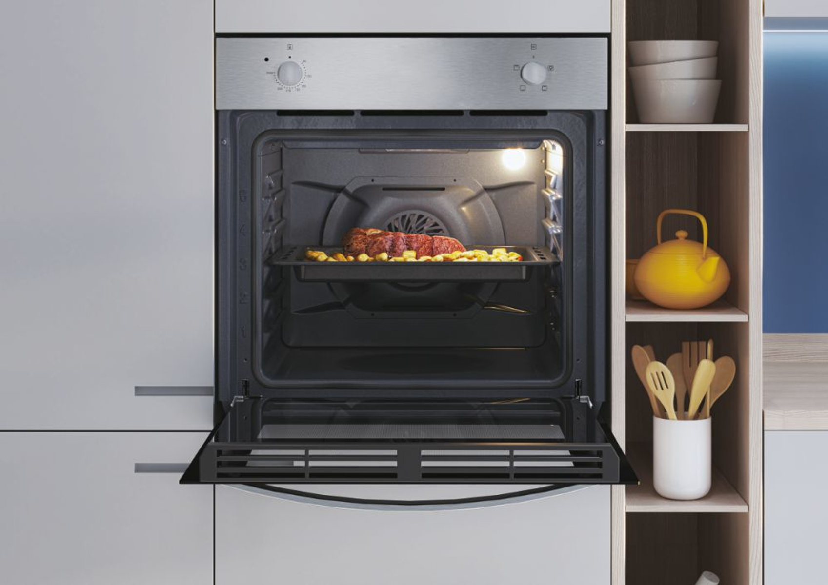 Un forno aperto con un vassoio di patate arrosto e carne. Armadi e mensole bianche visibili.