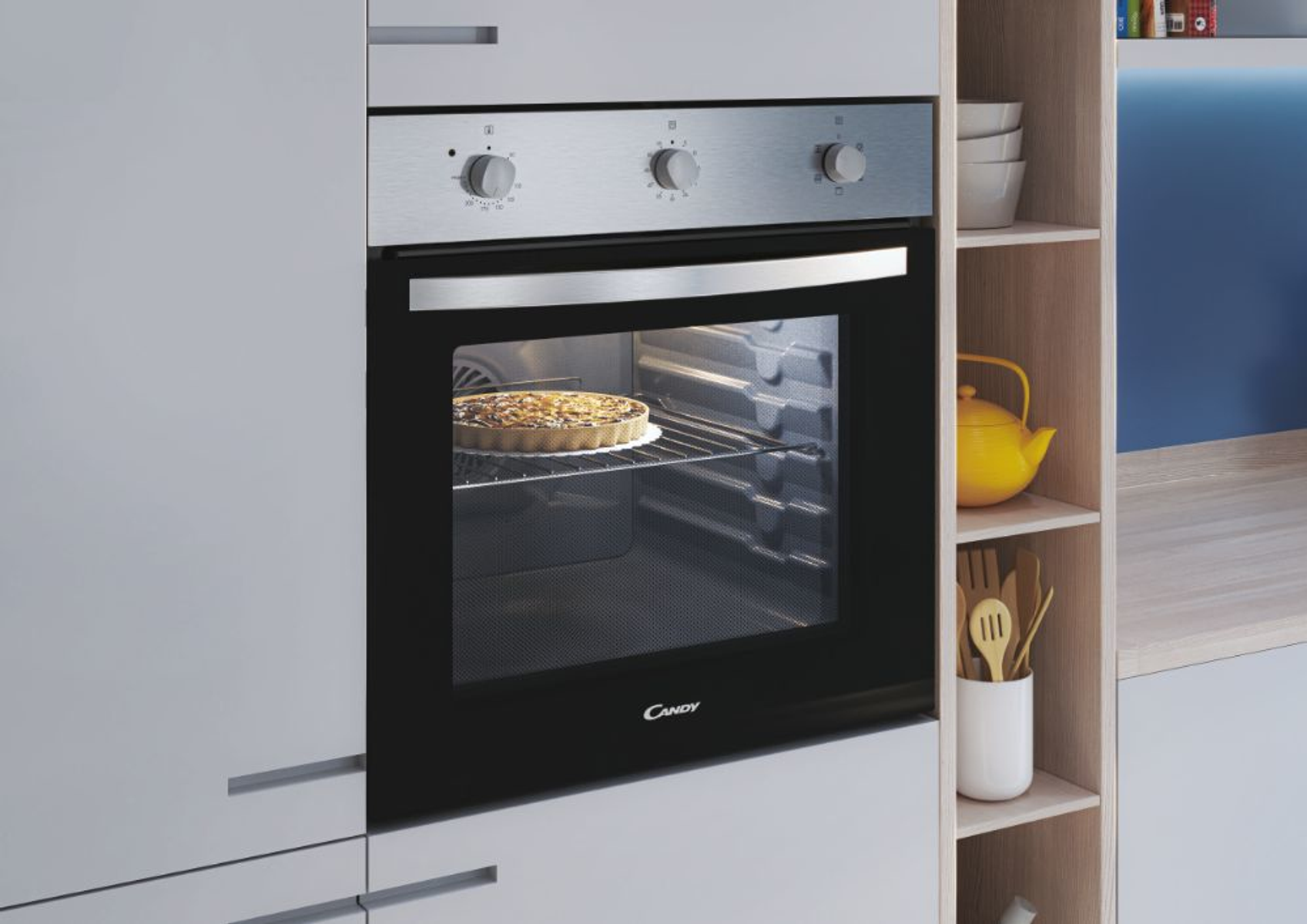 Forno Candy integrato in un mobile da cucina. Una torta cuoce all'interno del forno. Manopole frontali.