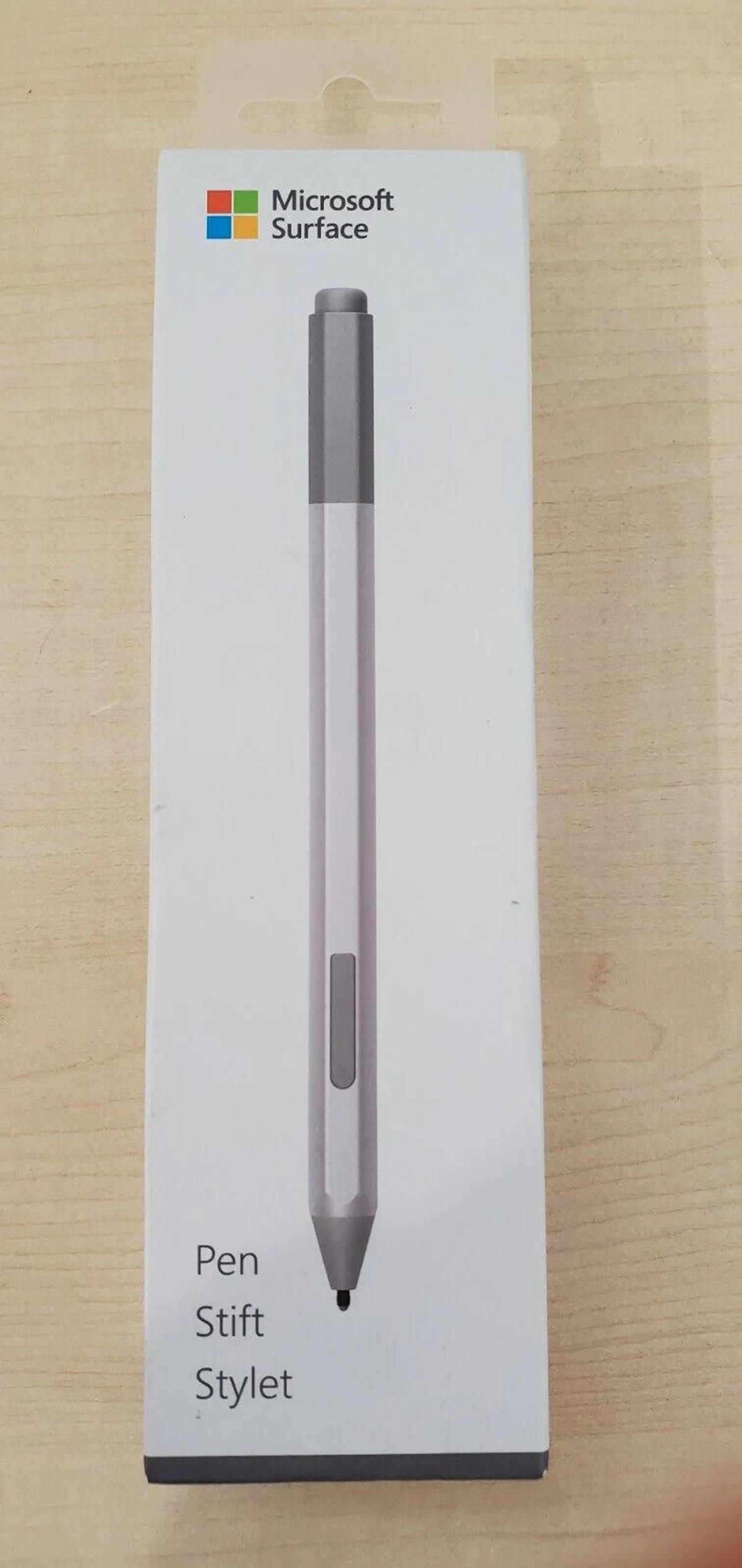 Stylet Microsoft Surface Pen dans son emballage, sur une surface en bois clair.