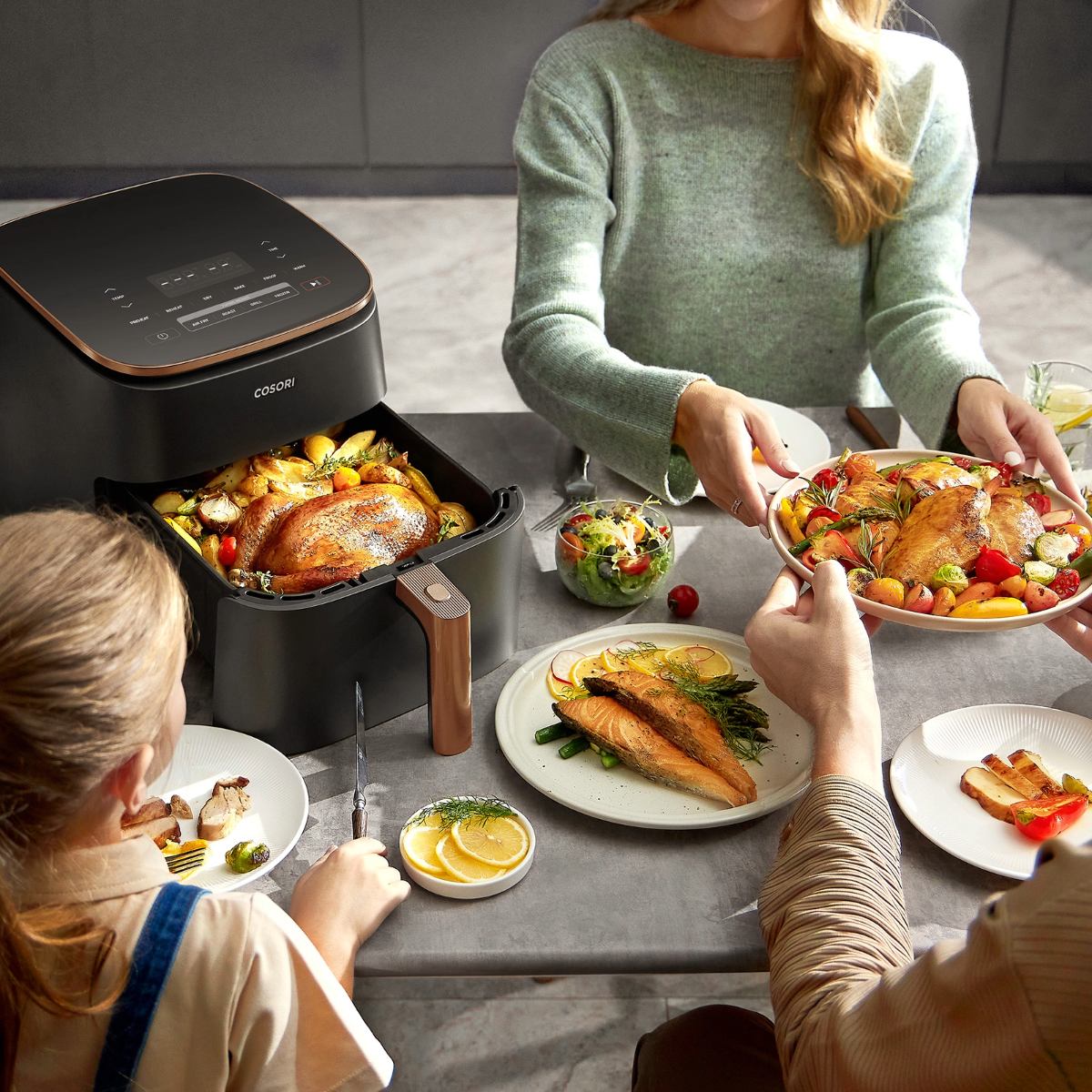 Ludzie przy stole z frytkownicą powietrzną, talerzami z jedzeniem i kobietą trzymającą talerz.