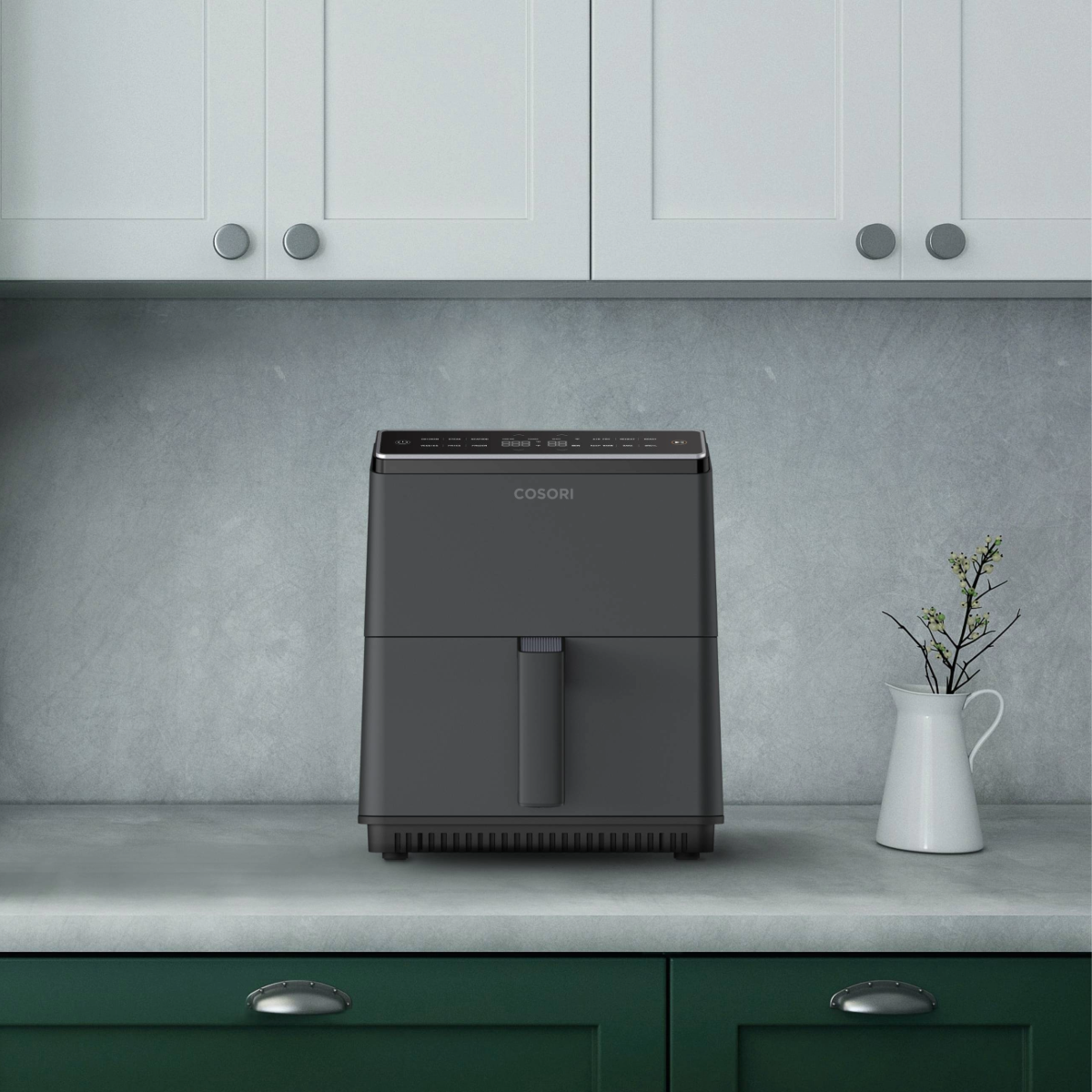 Czarna frytownica na blacie z białymi szafkami. Mały wazon z kwiatami obok.