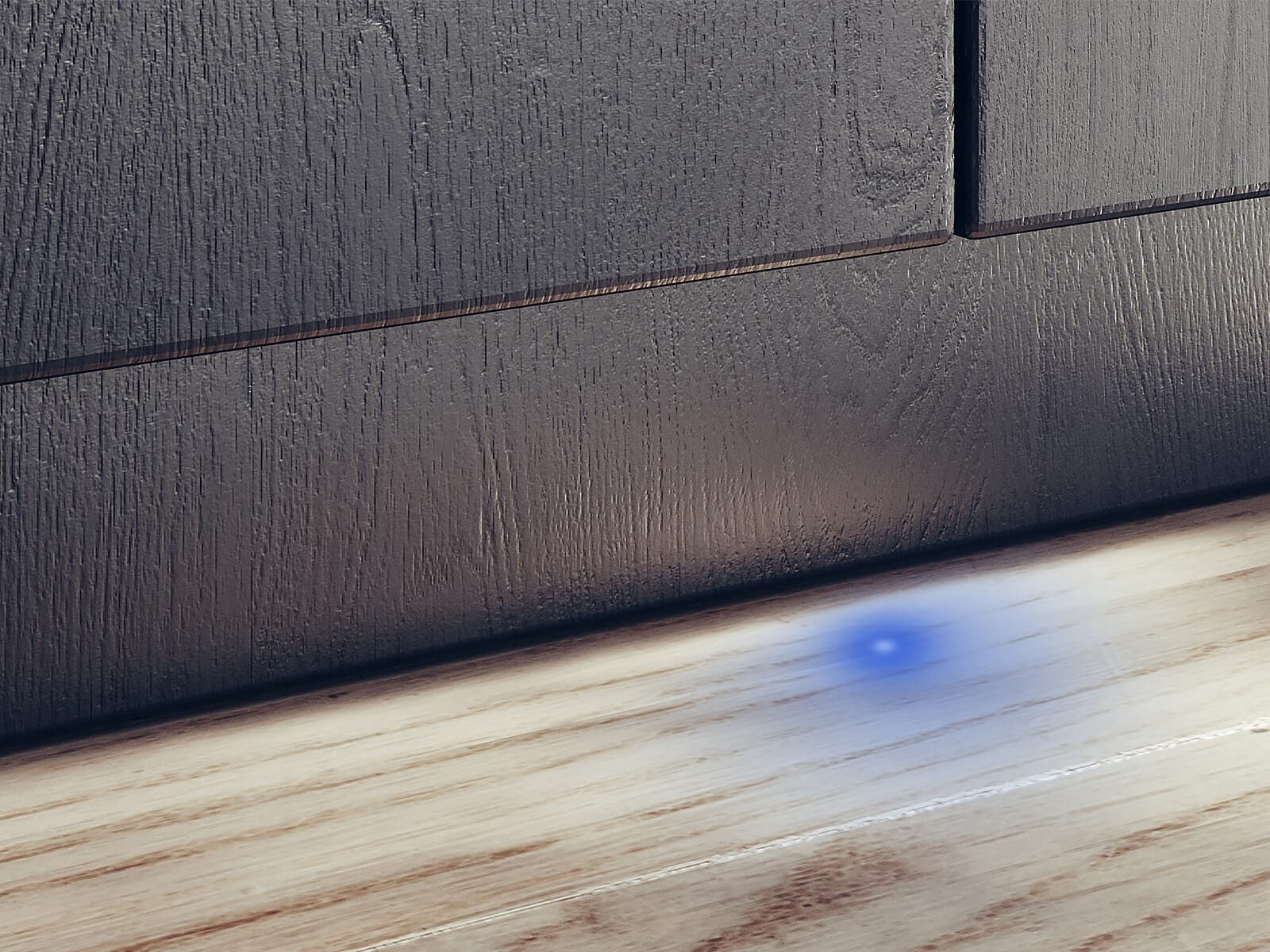 Pavimento in legno con una luce blu che brilla dal basso di un mobile in legno scuro.