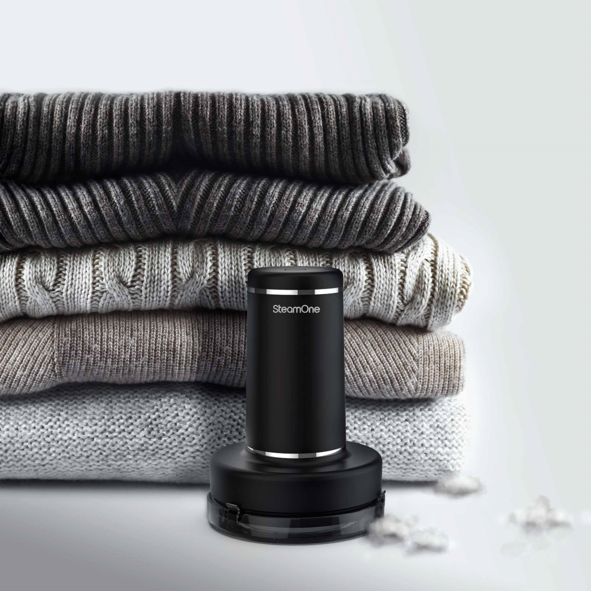 Défroisseur noir à côté d'une pile de pulls pliés dans diverses nuances de gris.