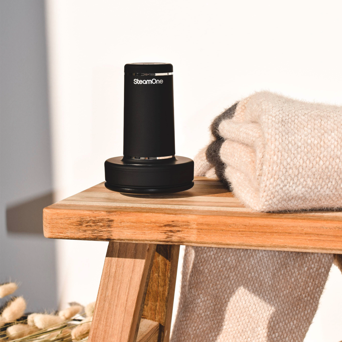 Nettoyeur vapeur cylindrique noir sur une surface en bois, à côté d'une couverture pliée.