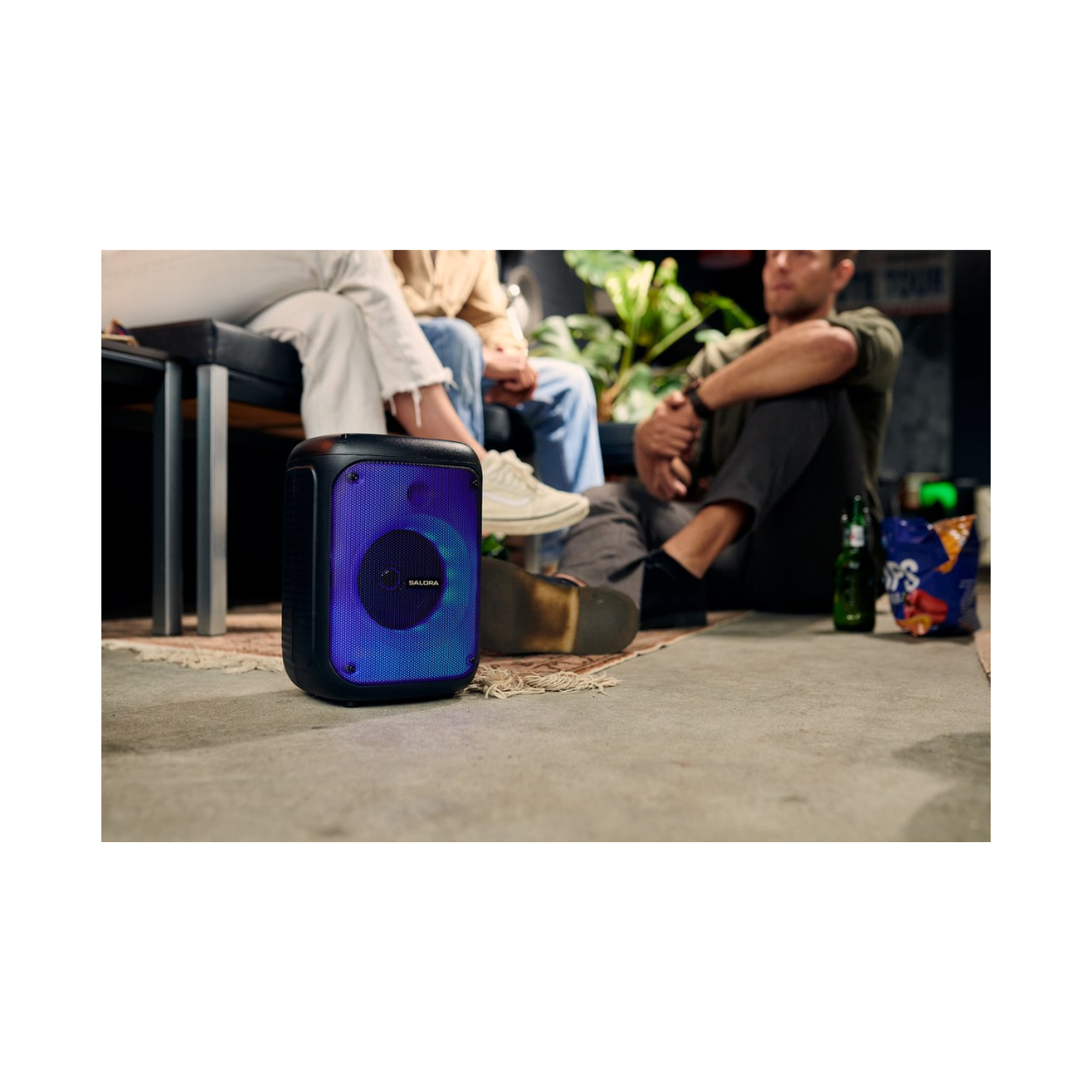Un haut-parleur noir avec une lumière bleue et violette est devant un groupe de personnes.