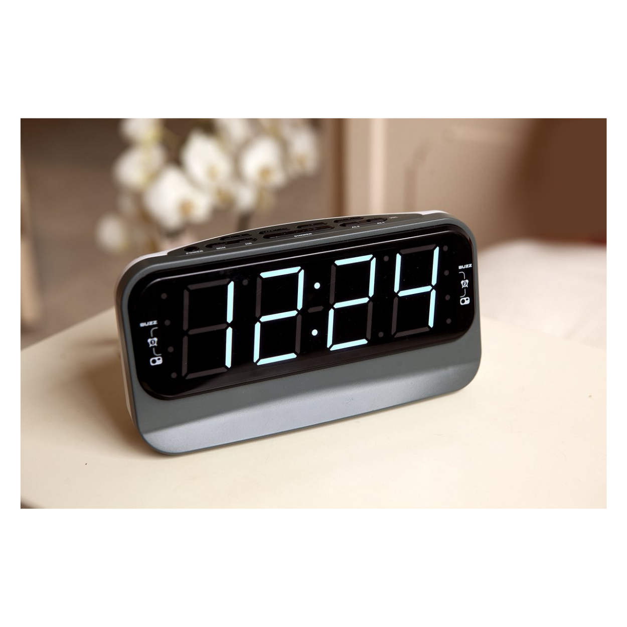 A digital clock shows 12:24 on a white surface. The clock is gray with black buttons.