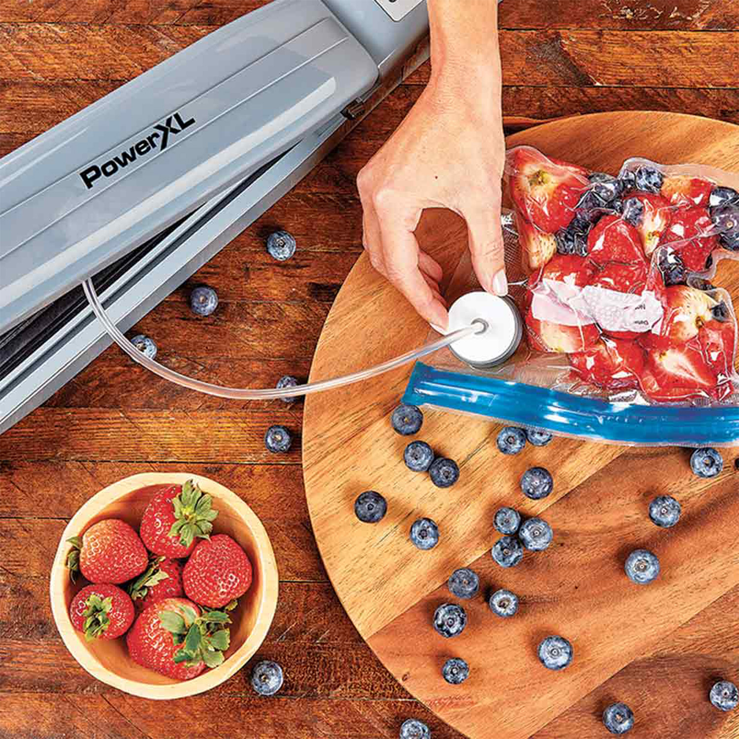 Eine Person versiegelt eine Tüte Erdbeeren und Blaubeeren mit einem Vakuumiergerät. Beeren auch in einer Schüssel.