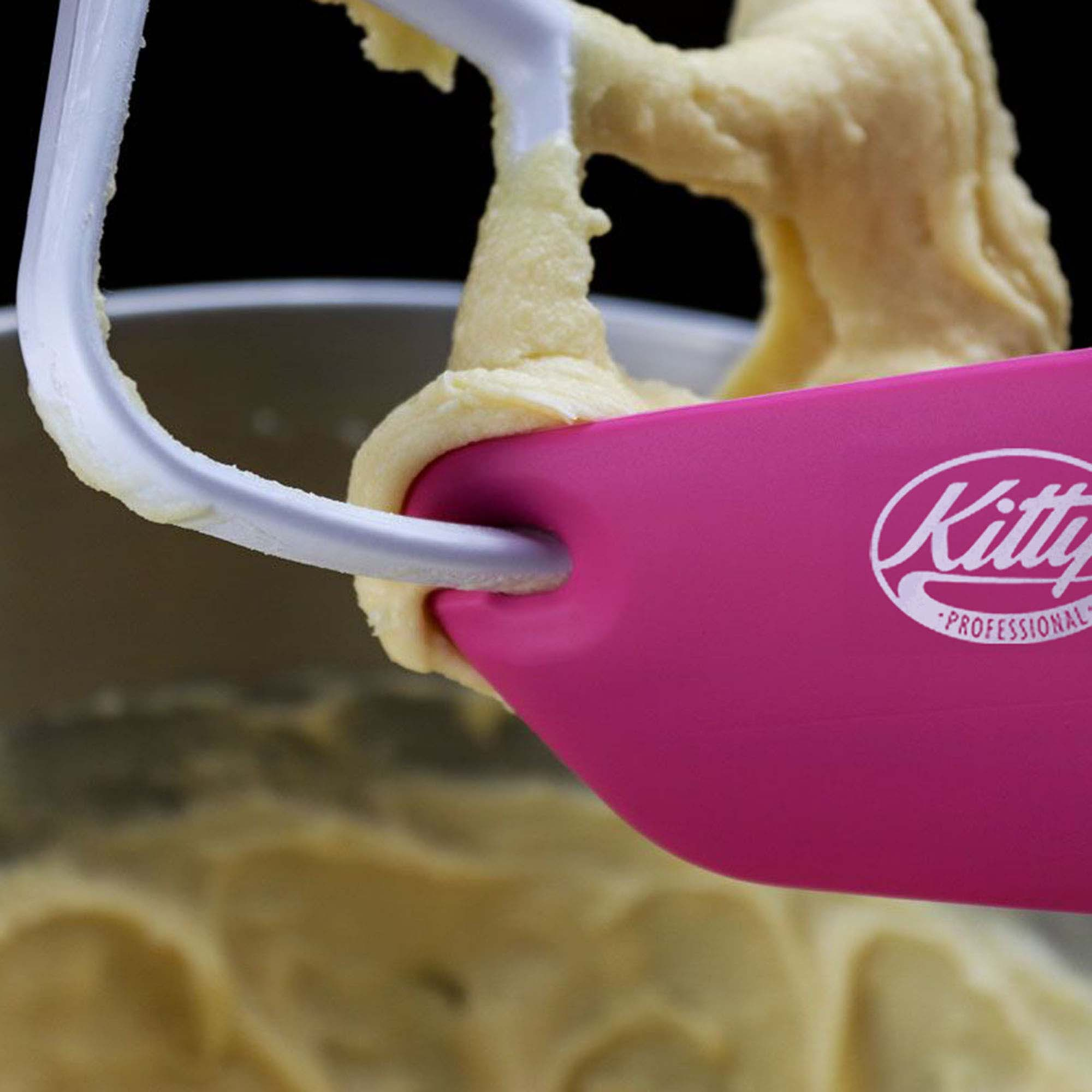 Ein rosa Spatel mit "Kitty Professional" kratzt Teig von einem Mixerarm ab, Nahaufnahme.
