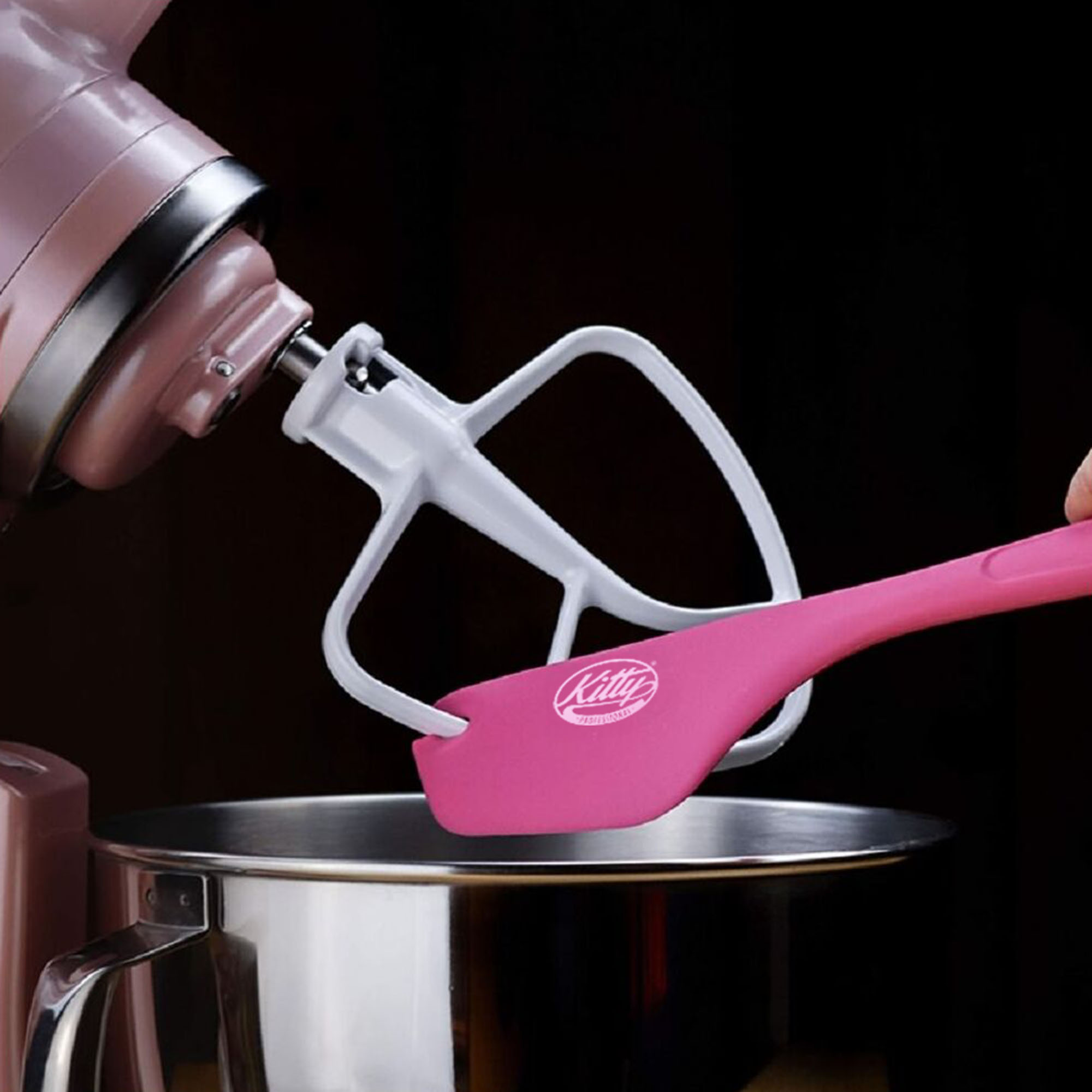 Ein rosa Küchenmixer mit weißem Rührbesen und pinkfarbenem Spatel, vor dunklem Hintergrund.