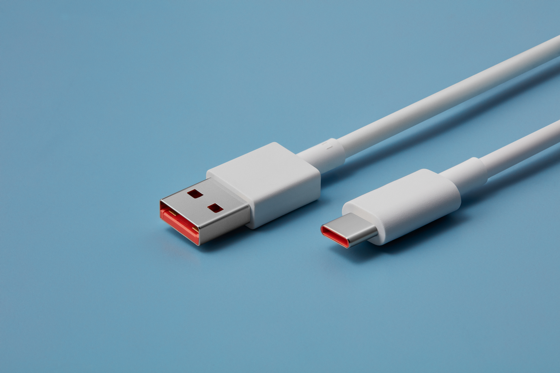 Biały kabel USB-C z czerwonymi złączami, leżący na jasnoniebieskiej powierzchni.