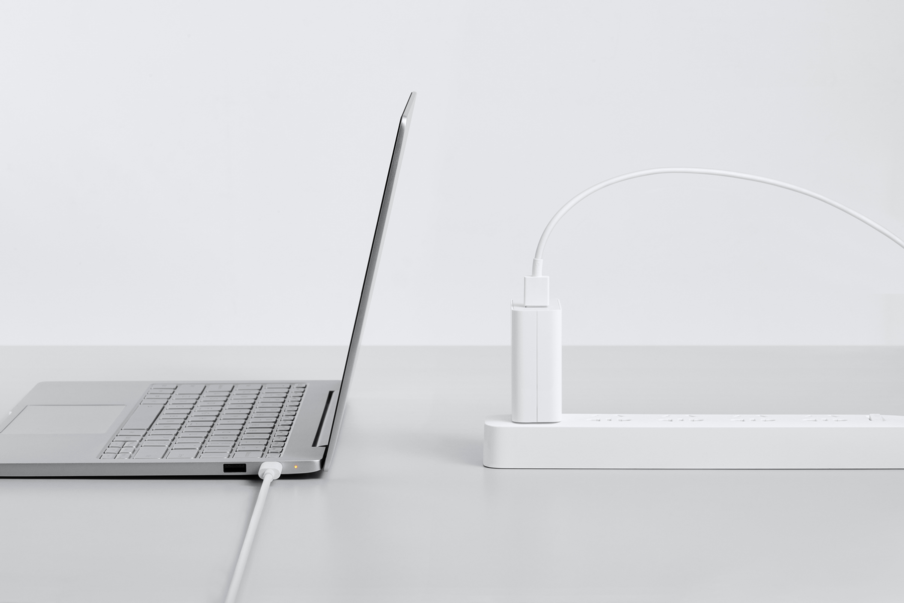Laptop podłączony do białej listwy zasilającej. Biała ładowarka jest podłączona do laptopa.