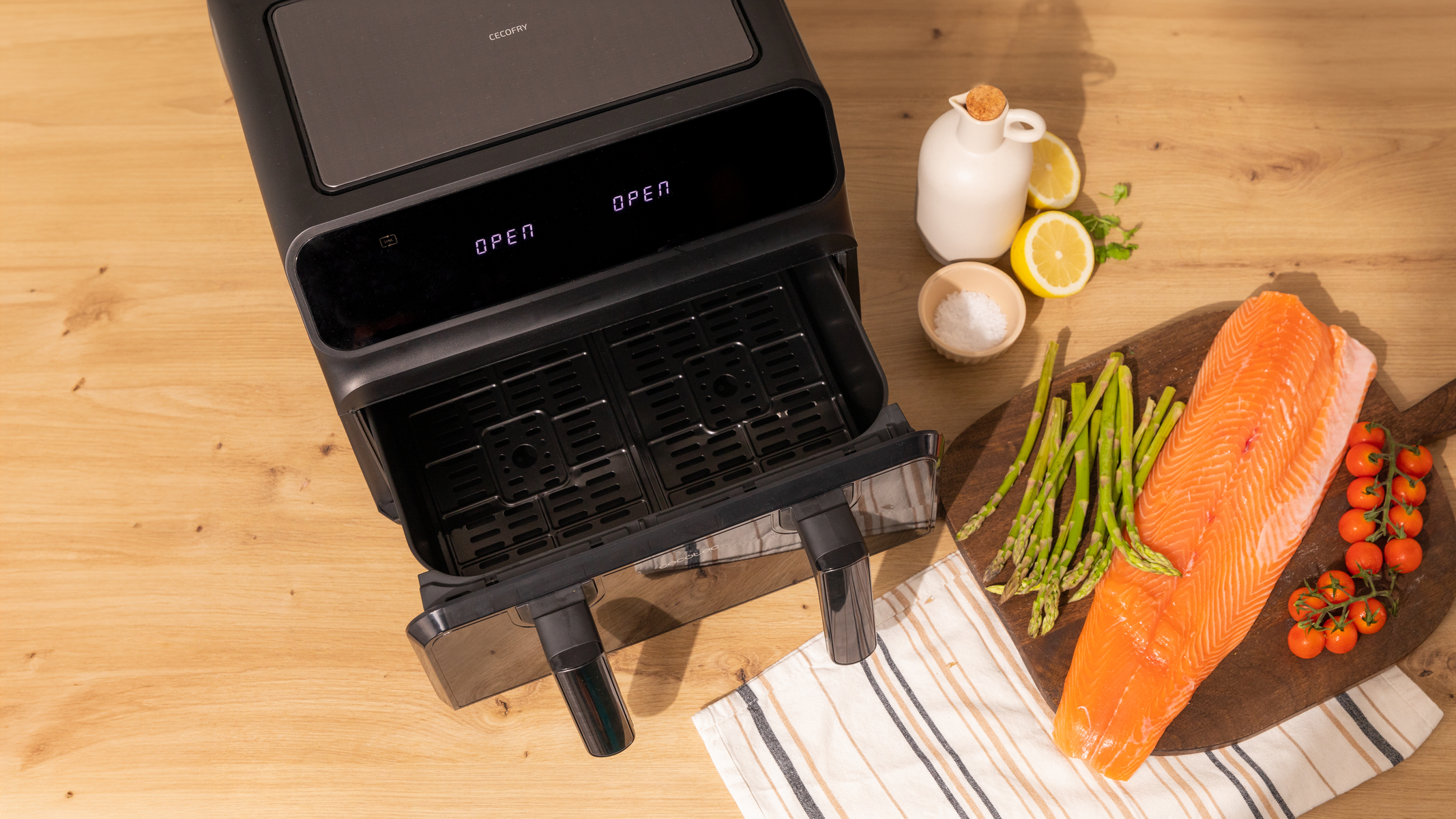 Frytownica beztłuszczowa z otwartą szufladą, łosoś, szparagi, pomidory i olej na drewnie.