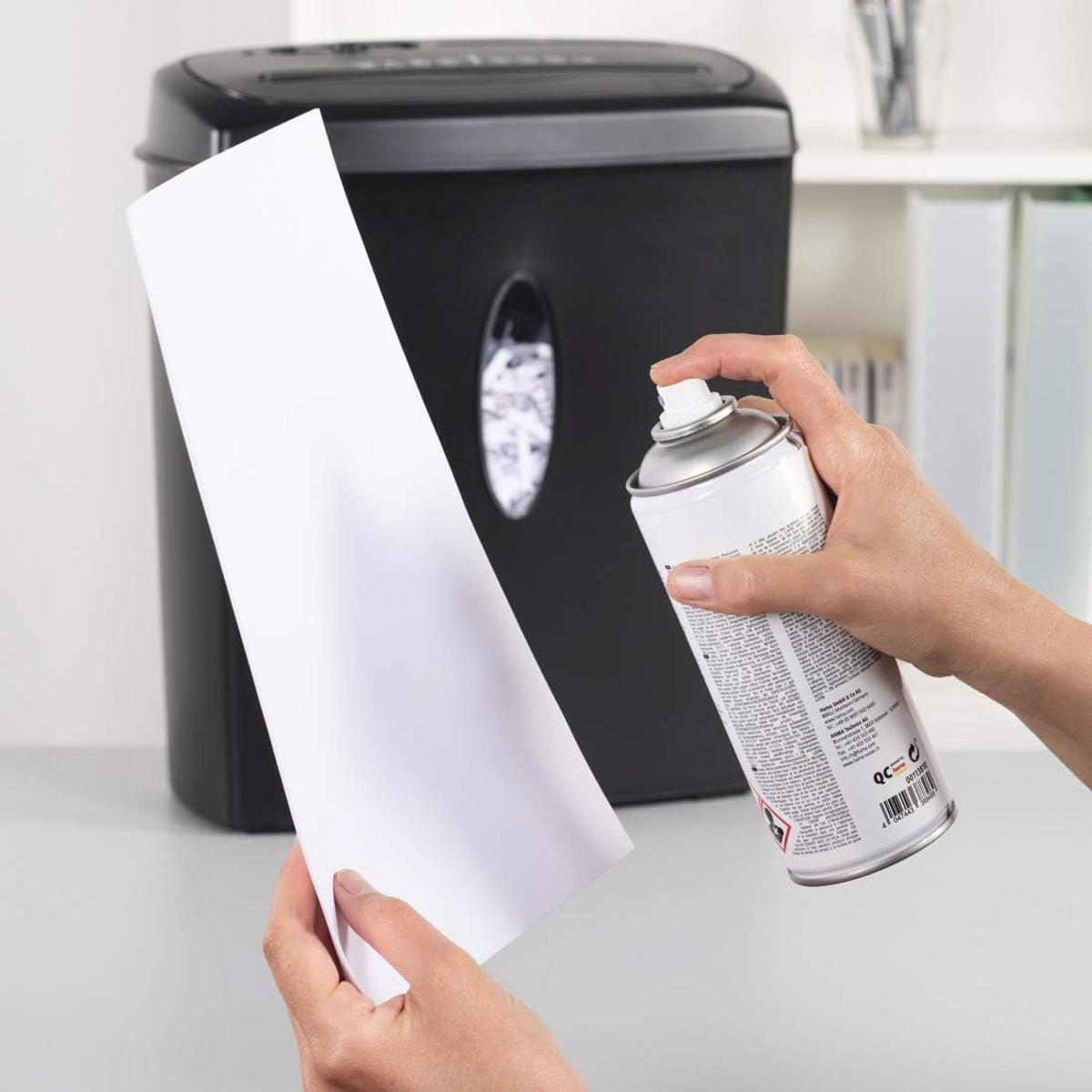 Osoba spryskuje kartkę papieru przed czarną niszczarką.