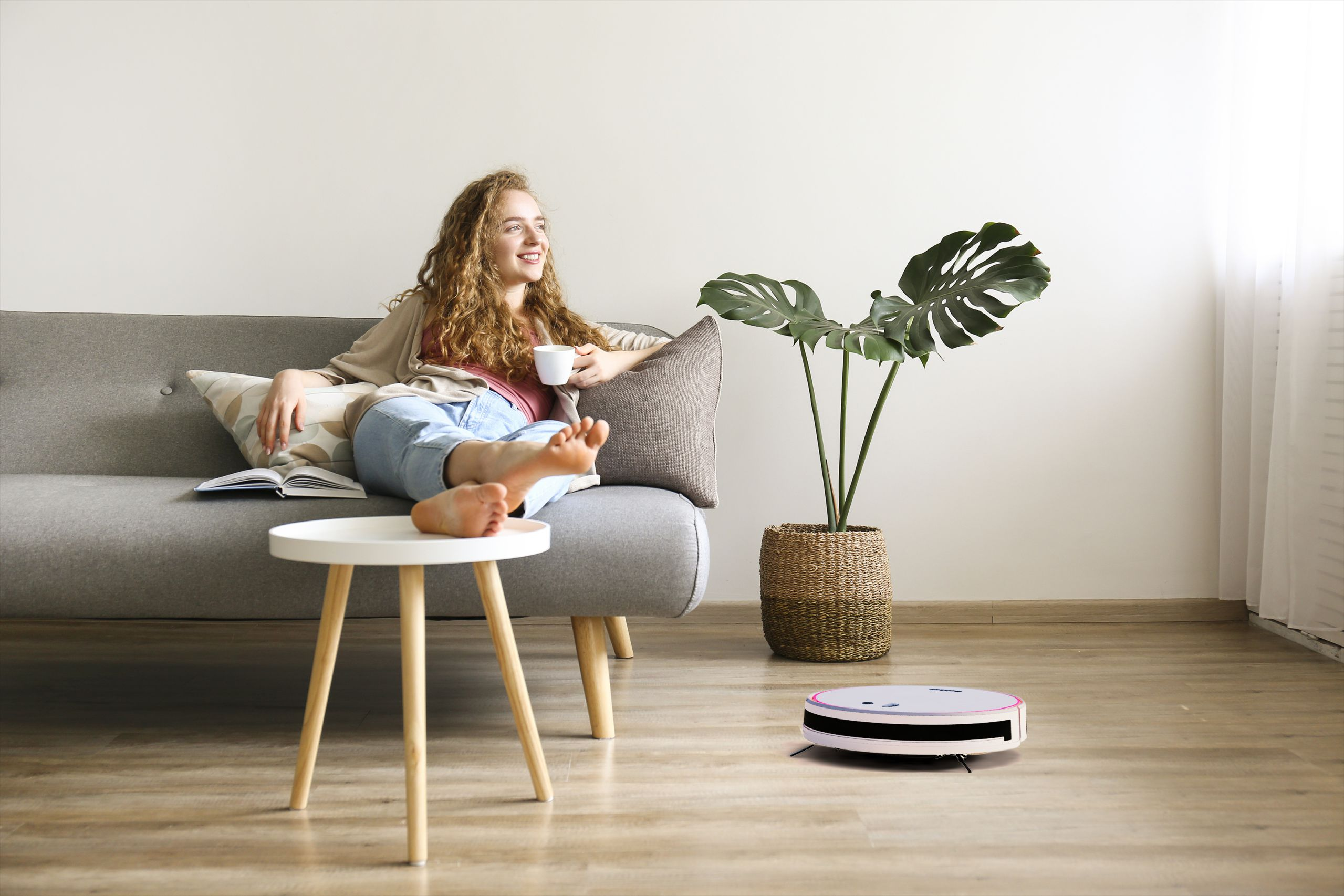 Frau auf Sofa mit Buch, Roboter-Staubsauger reinigt den Boden, Pflanze.