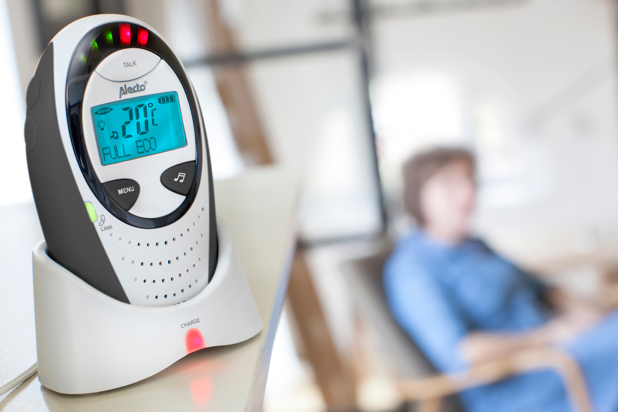 Niania elektroniczna z wyświetlaczem pokazuje 20 stopni Celsjusza. Kobieta jest w rozmytym tle.