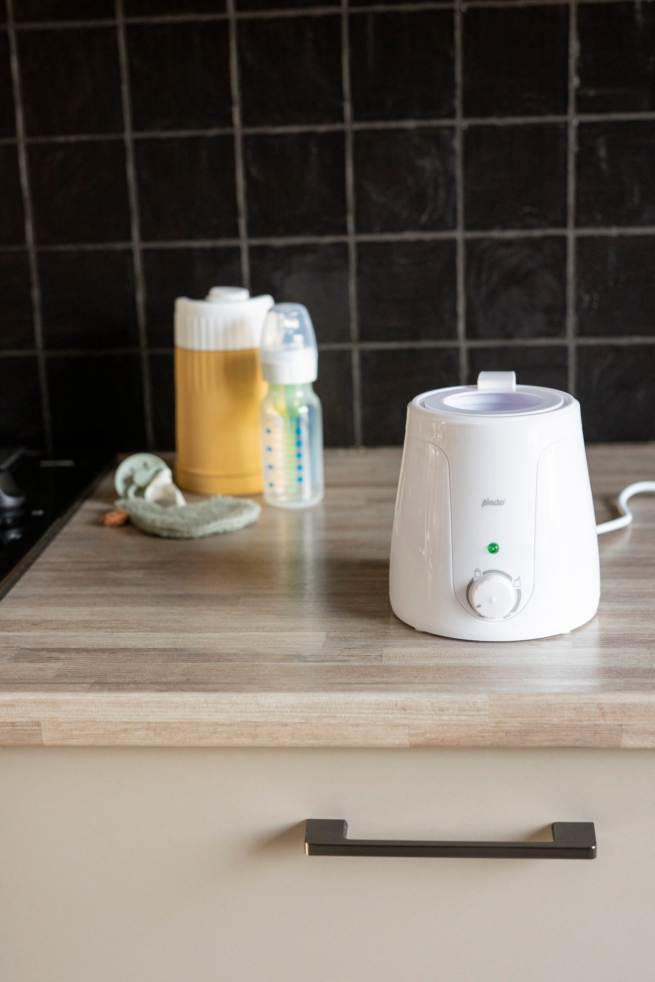 Podgrzewacz do butelek i butelki na drewnianym blacie, z czarnym tłem z płytek.