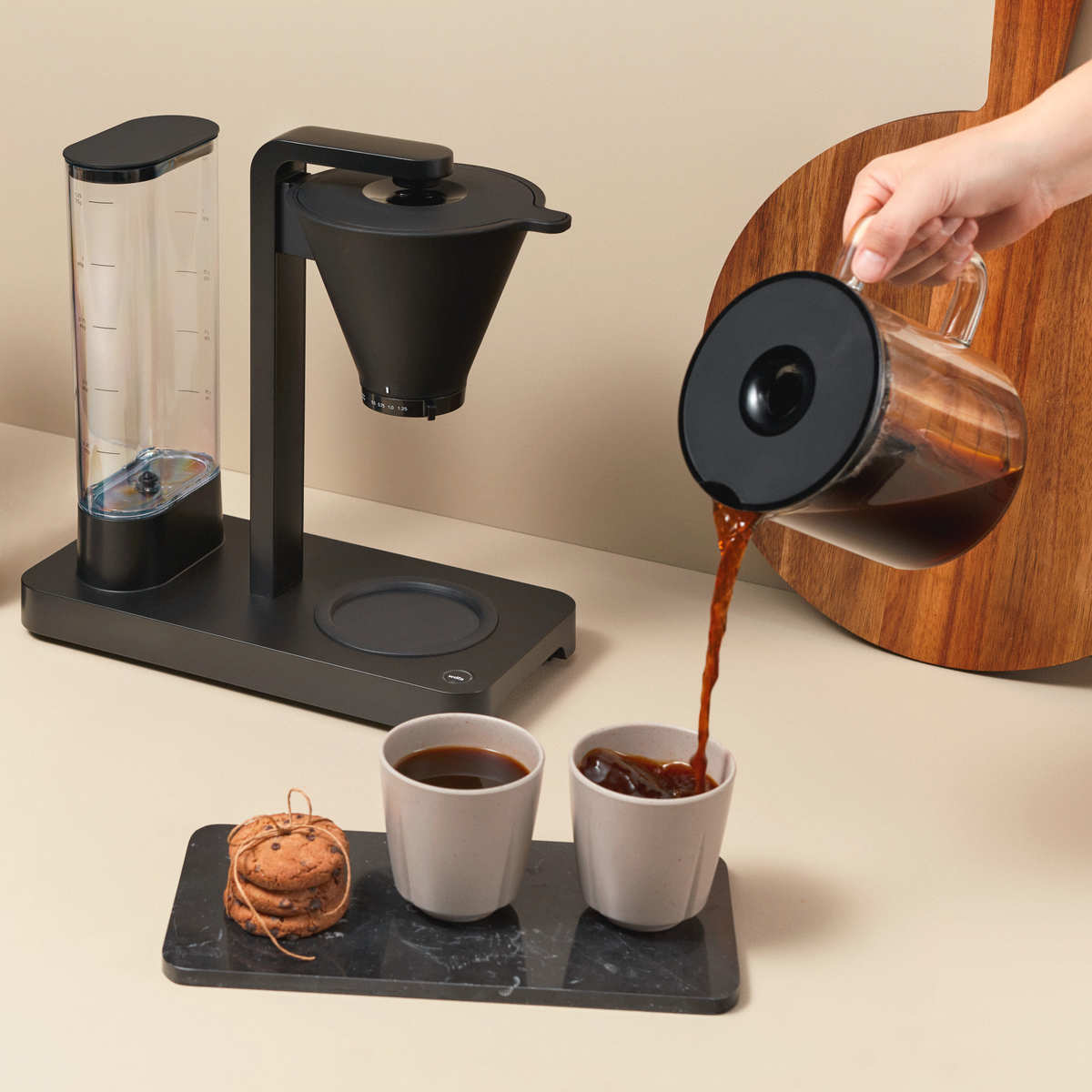Caffè versato in una tazza. Macchina per il caffè a sinistra, biscotti e una tazza di caffè su un vassoio, tagliere a destra.