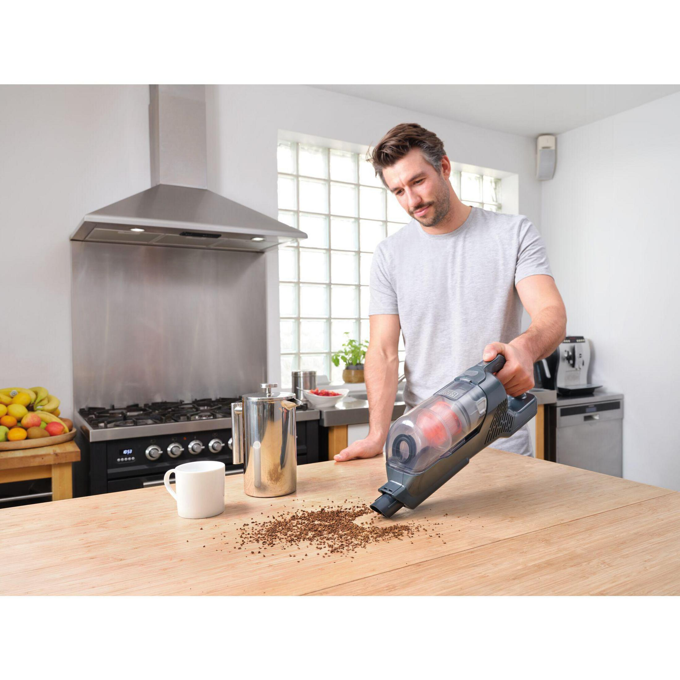 Un uomo aspira fondi di caffè rovesciati da un tavolo di legno in una cucina. Una caffettiera è nelle vicinanze.