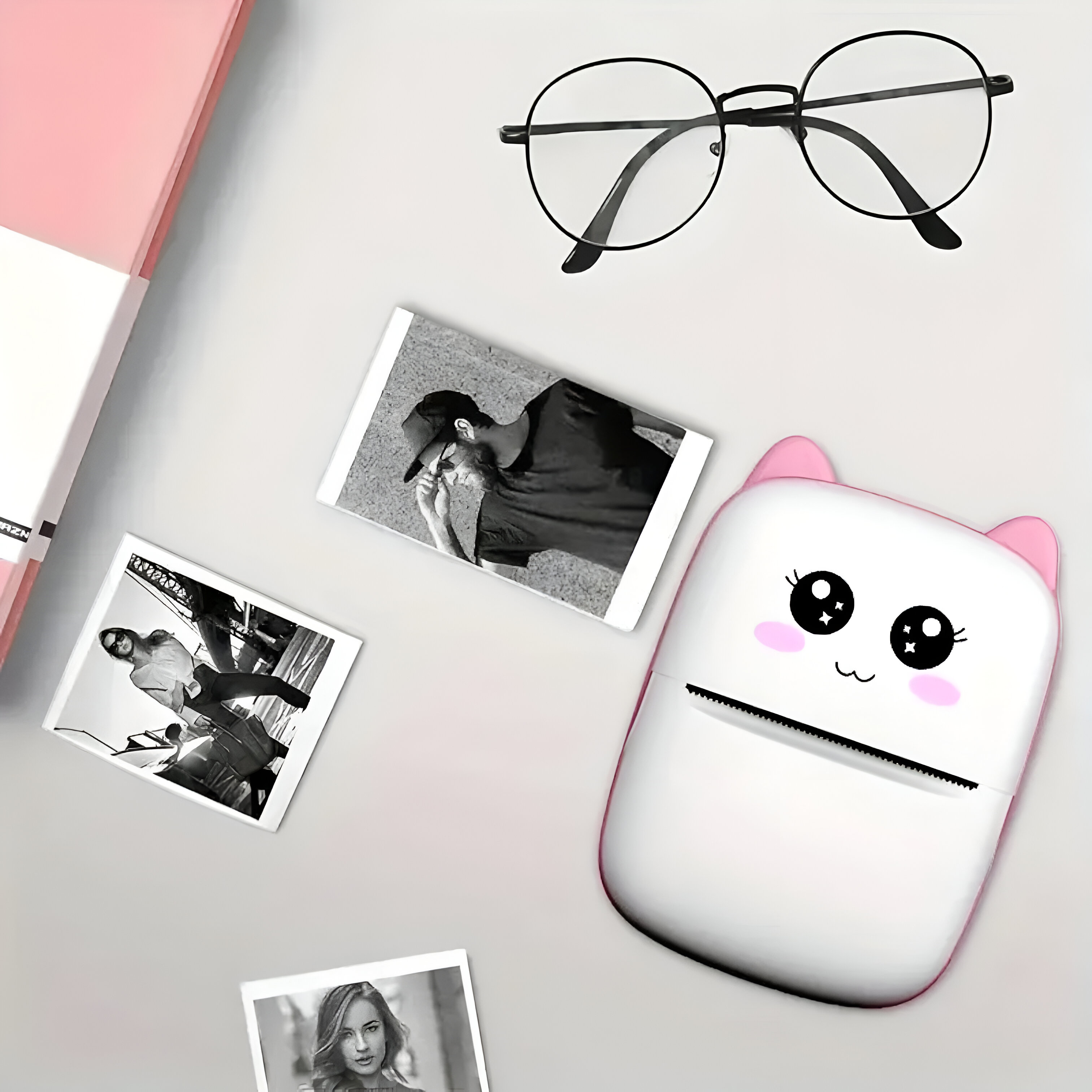 Fotos y una linda impresora blanca con orejas rosadas sobre una superficie clara, con gafas y una caja.