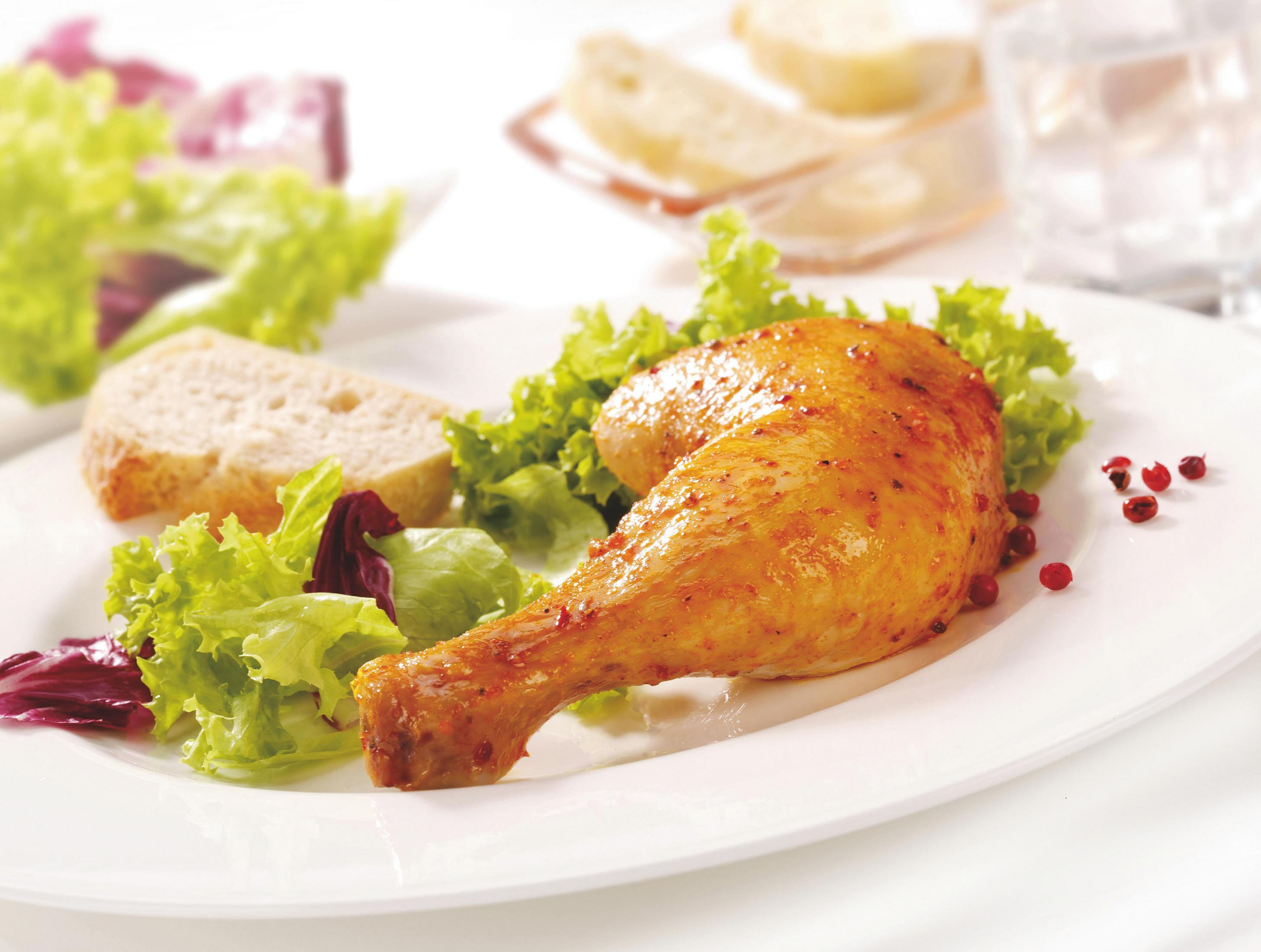 Coscia di pollo arrosto con insalata e pane in un piatto bianco.