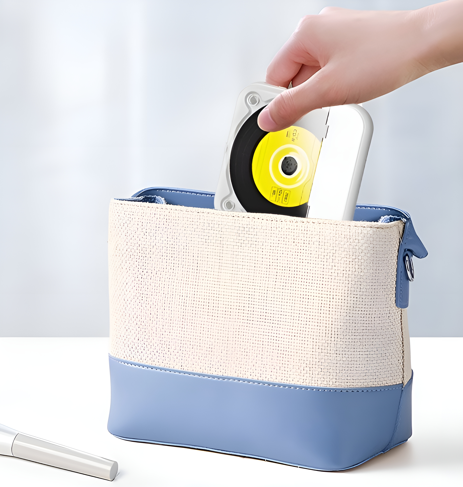 Eine Hand legt eine gelbe CD in eine kleine, weiß-blaue Handtasche. Die CD ist sichtbar.