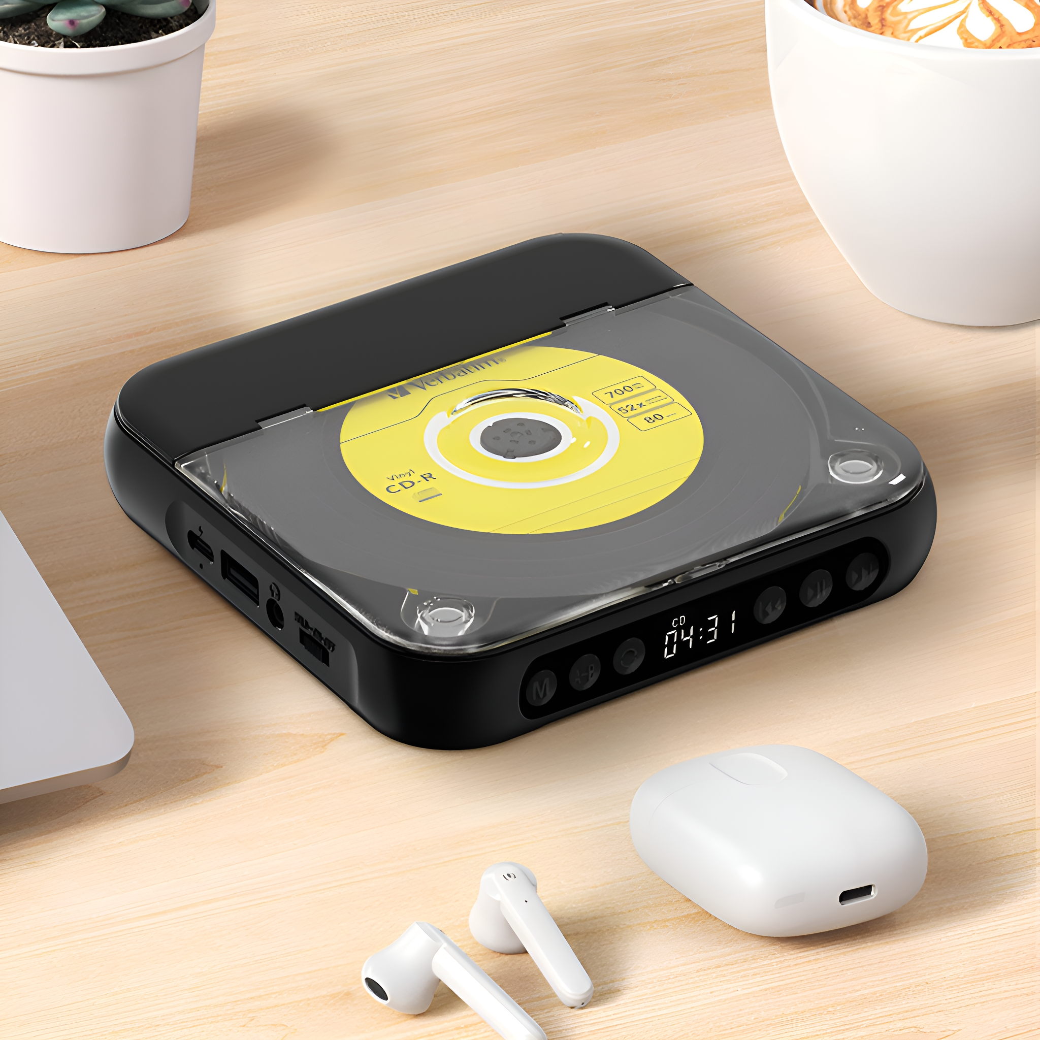 Ein schwarzer CD-Player mit transparentem Deckel auf einem Holztisch. Weiße Kopfhörer und eine weiße Tasse.