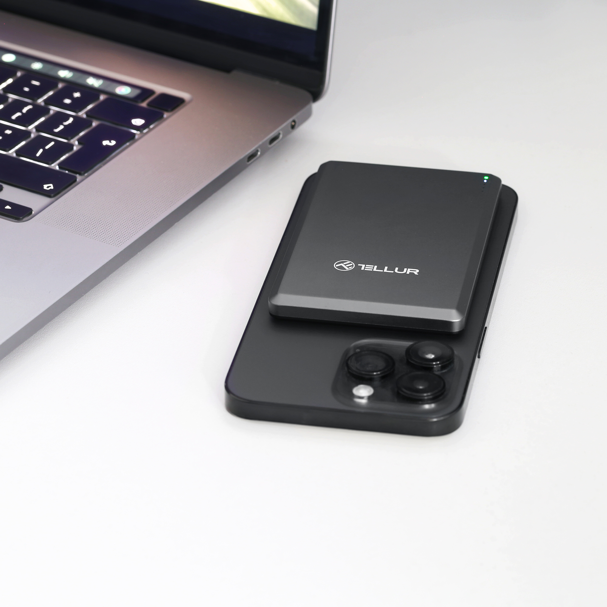 Czarny telefon z czarną ładowarką umieszczono na białym stole obok laptopa.