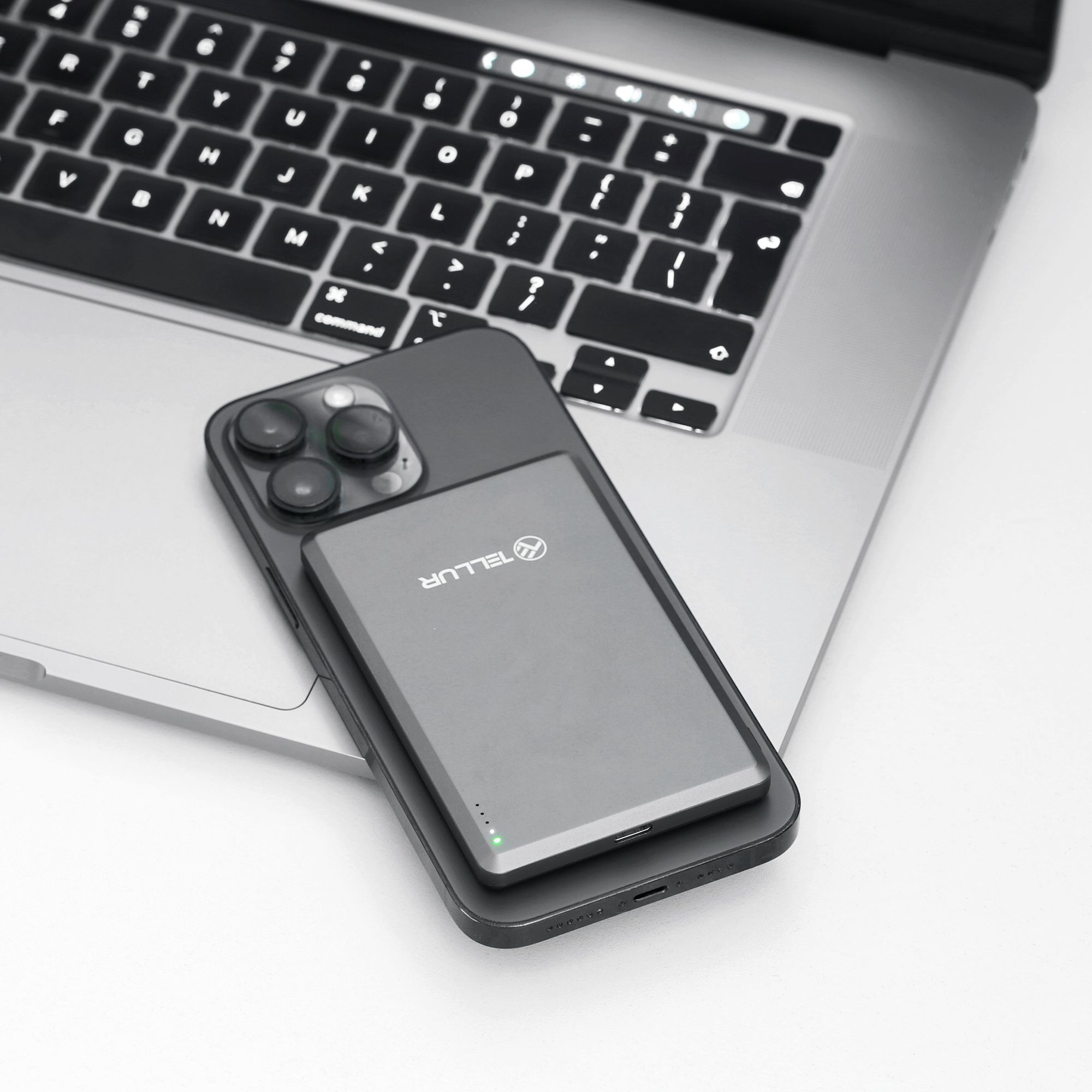 Szary telefon spoczywający na laptopie. Szara przenośna ładowarka znajduje się na telefonie.