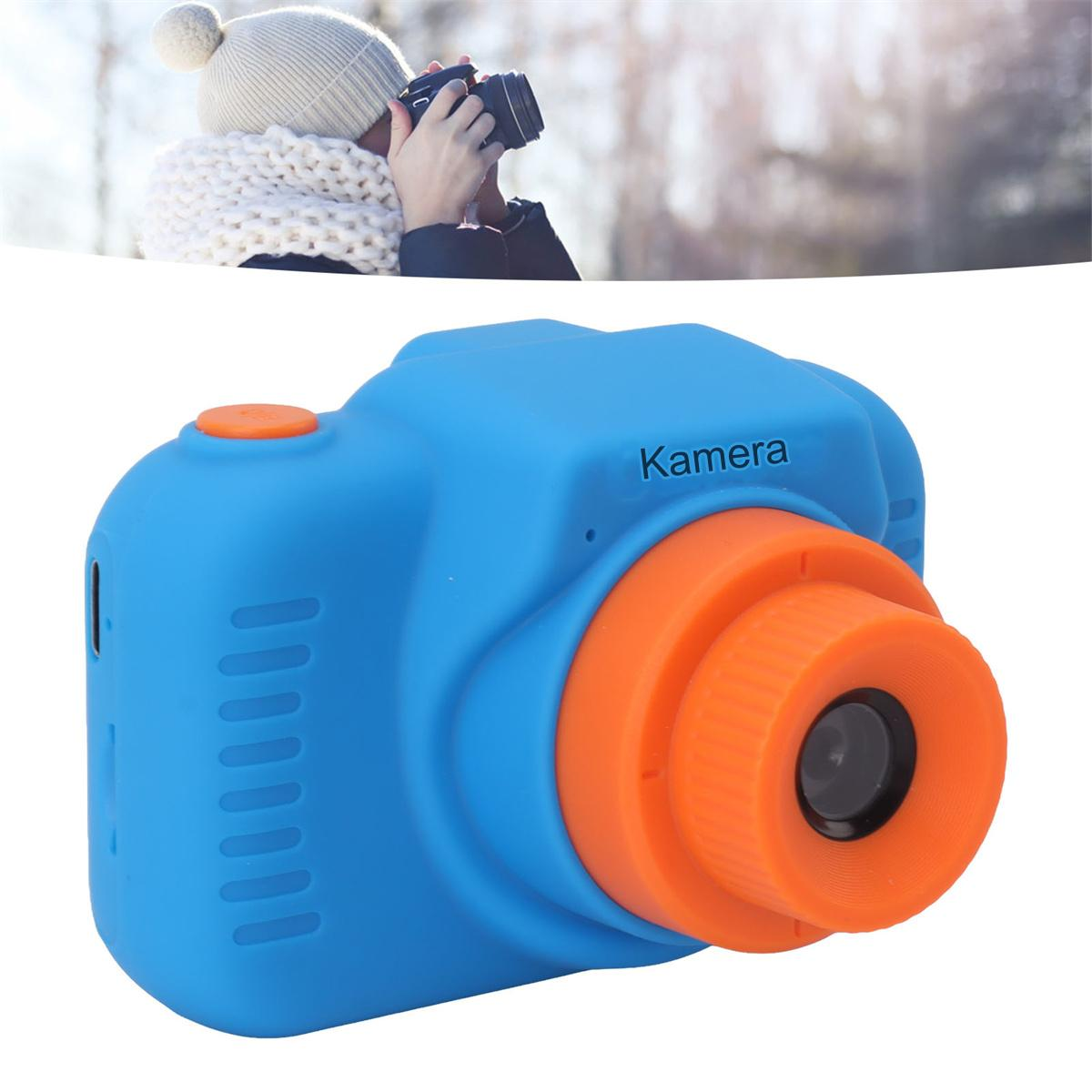 Blaue und orangefarbene Spielzeugkamera, gehalten von einer Person mit weißem Schal und Hut im Hintergrund.