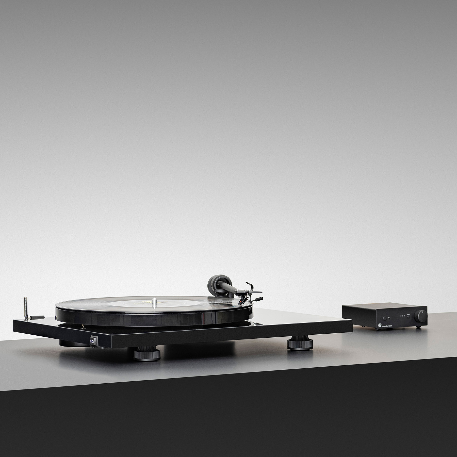 Czarny gramofon i wzmacniacz na czarnej powierzchni. Biało-szare gradientowe tło.