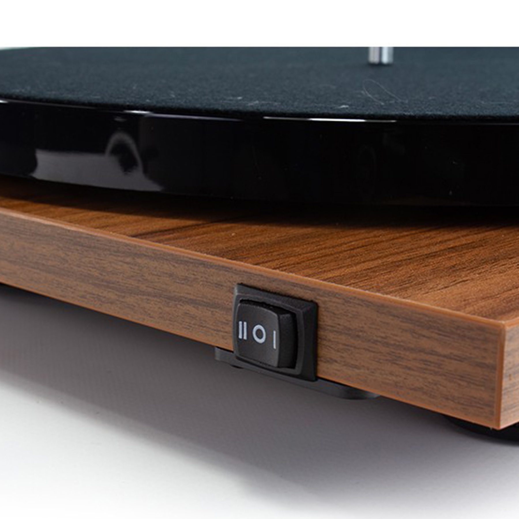 Zbliżenie drewnianej powierzchni z czarną podstawą gramofonu i włącznikiem/wyłącznikiem. Białe tło.