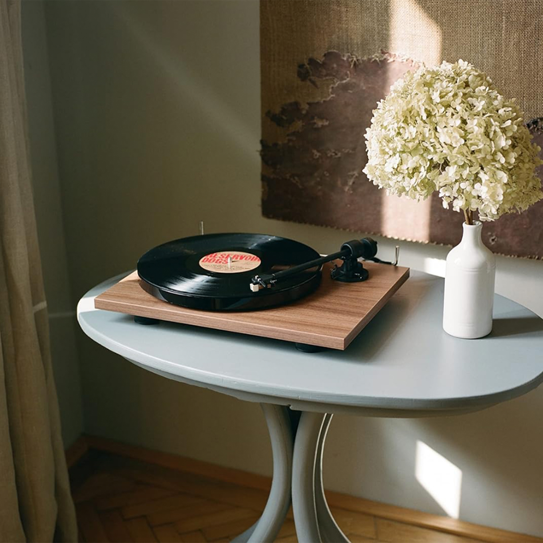 Gramofon z płytą winylową na drewnianej powierzchni, białe kwiaty i sztuka abstrakcyjna.