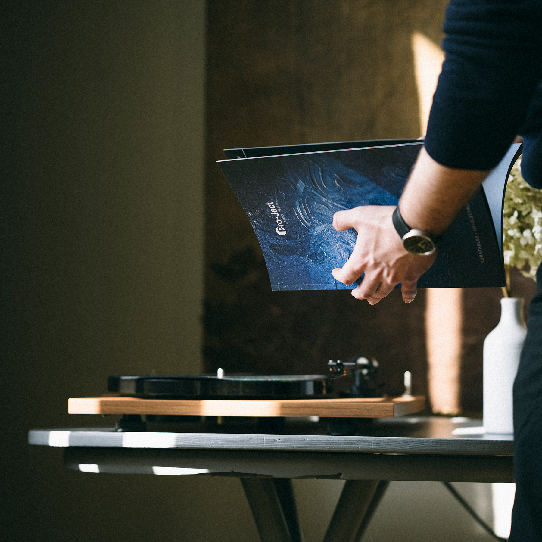 Ręce osoby trzymającej płytę winylową nad gramofonem na stole i biały wazon.