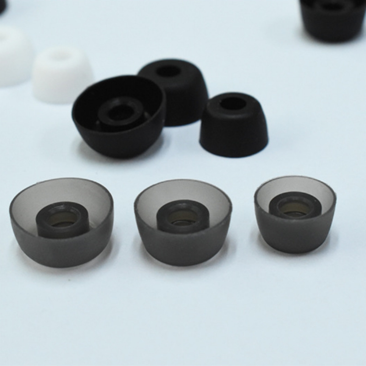 Różne rozmiary czarnych i szarych wkładek dousznych do słuchawek. Na białej powierzchni.