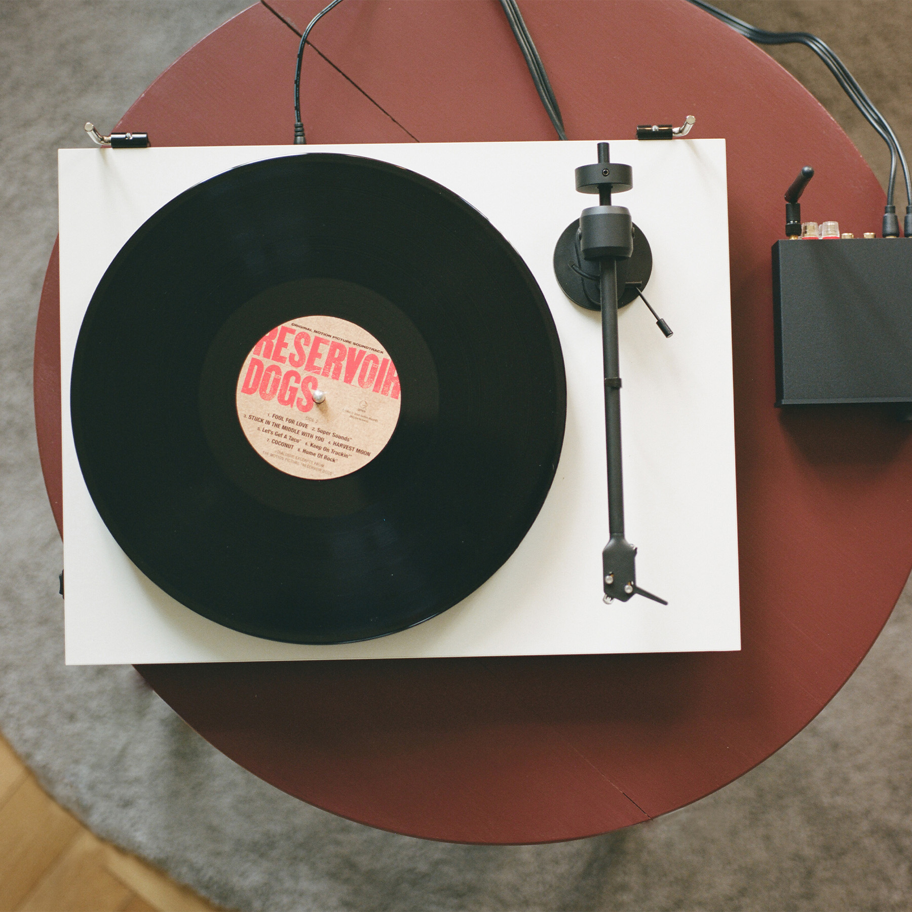 Plattenspieler mit schwarzer Vinyl-Schallplatte. Roter Tischhintergrund. Schwarzer Verstärker rechts.