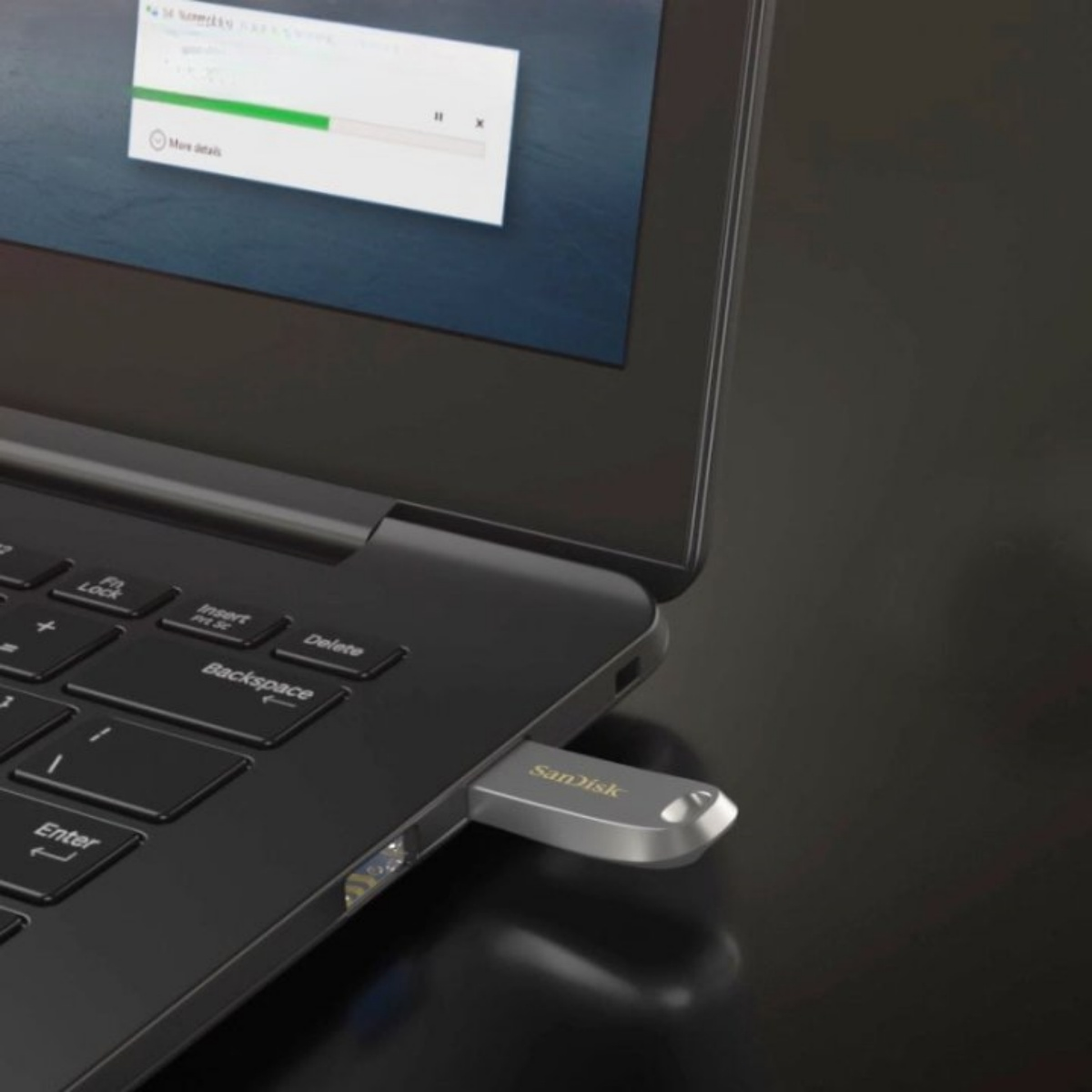 Ein silberner Sandisk USB-Stick, der an einen Laptop angeschlossen ist. Der Laptop-Bildschirm zeigt eine Dateiübertragung.