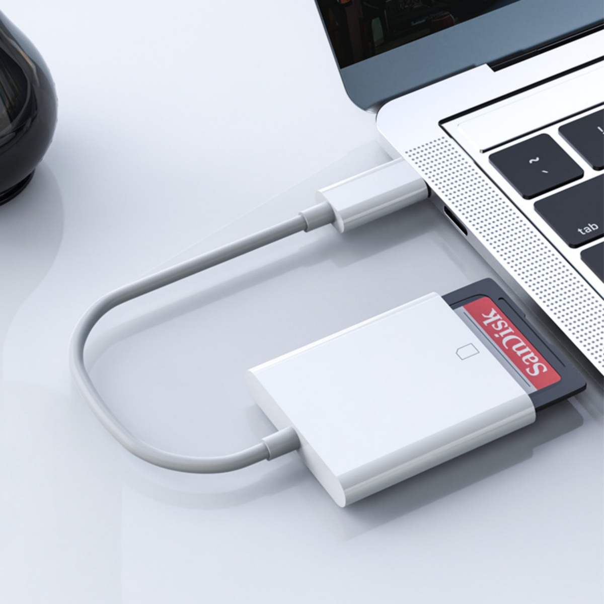 Weißer Kartenleser mit eingesetzter SanDisk SD-Karte, verbunden mit einem Laptop über ein weißes Kabel.