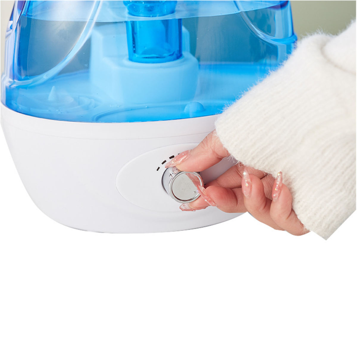 Eine Hand justiert einen Drehregler an einem weiß-blauen Luftbefeuchter, Wassertank sichtbar. Weißer Hintergrund.