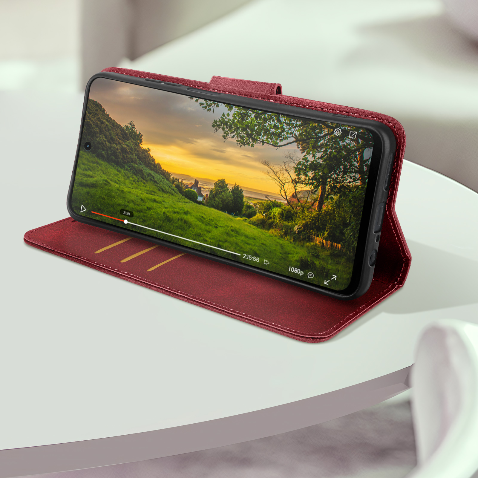Uno smartphone in una custodia rossa mostra un video di un paesaggio verde con un tramonto.