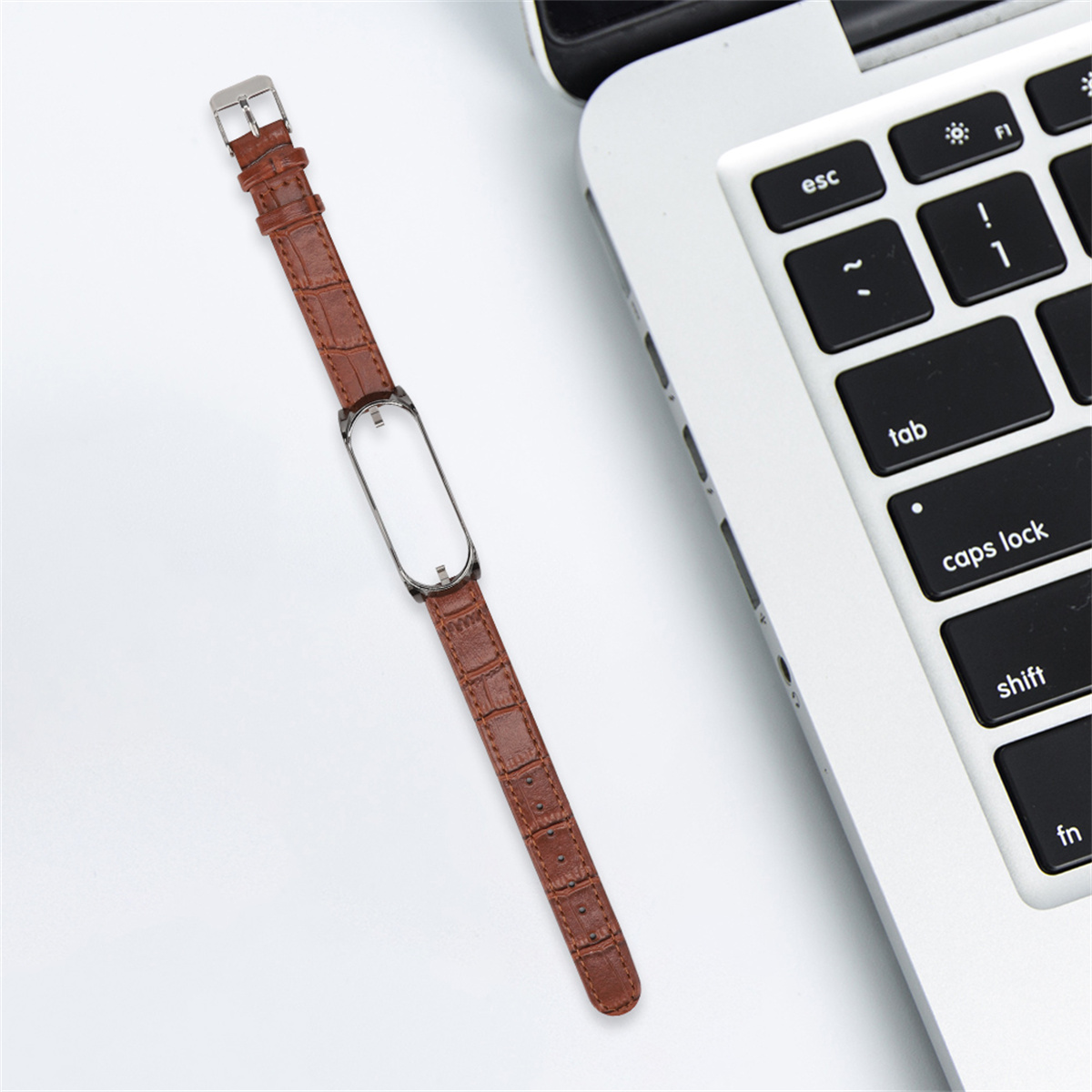 Ein braunes Smartwatch-Armband aus Leder liegt auf einer weißen Oberfläche neben einem offenen Laptop.
