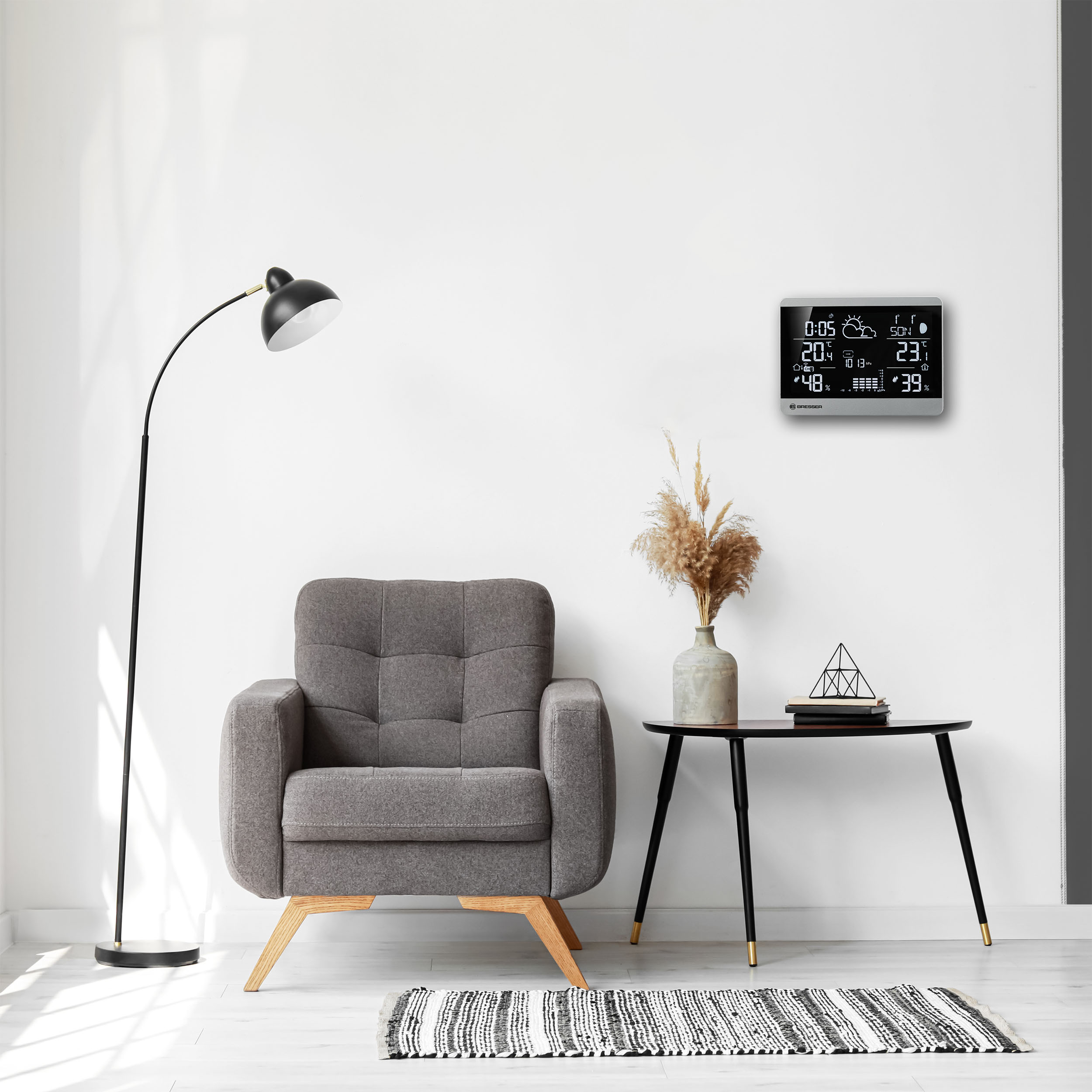 Escena de sala de estar: Sillón gris, lámpara, mesa con jarrón y estación meteorológica en pared.