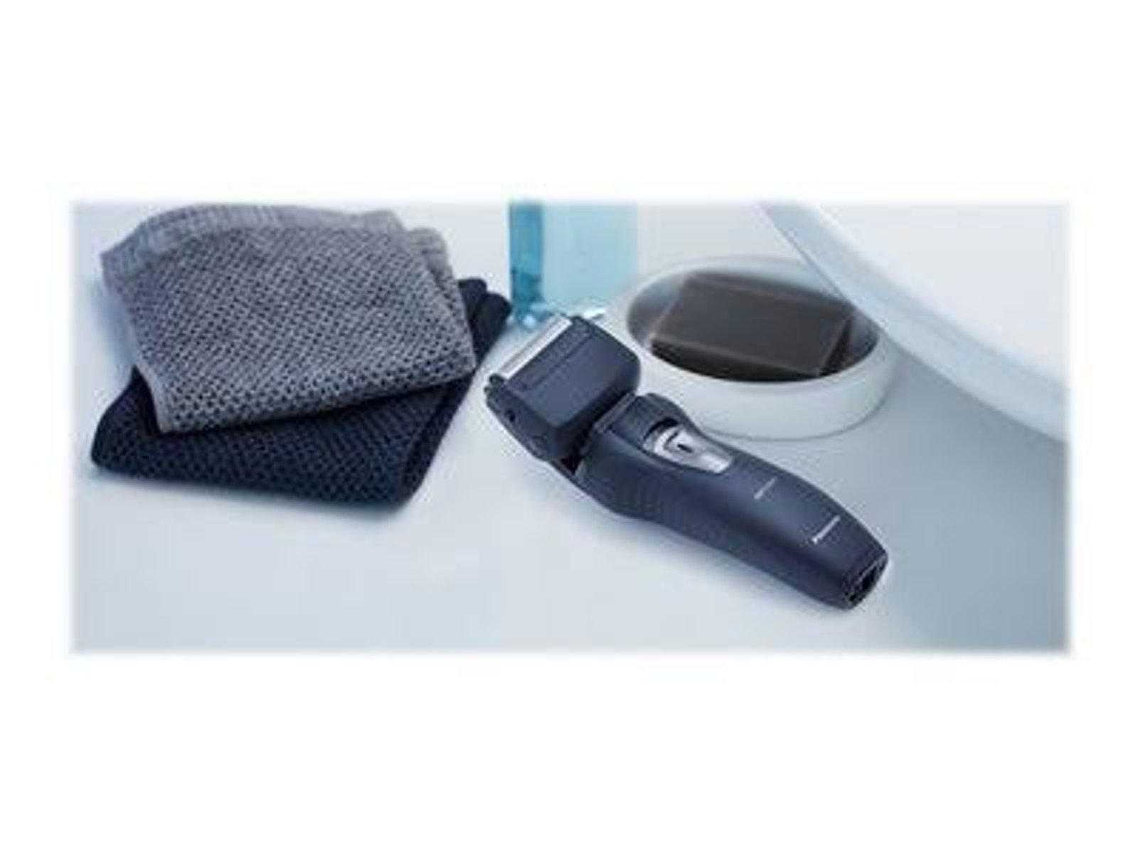 Trymer do brody na białej powierzchni z ręcznikami i mydłem. Niebieski płyn w butelce.