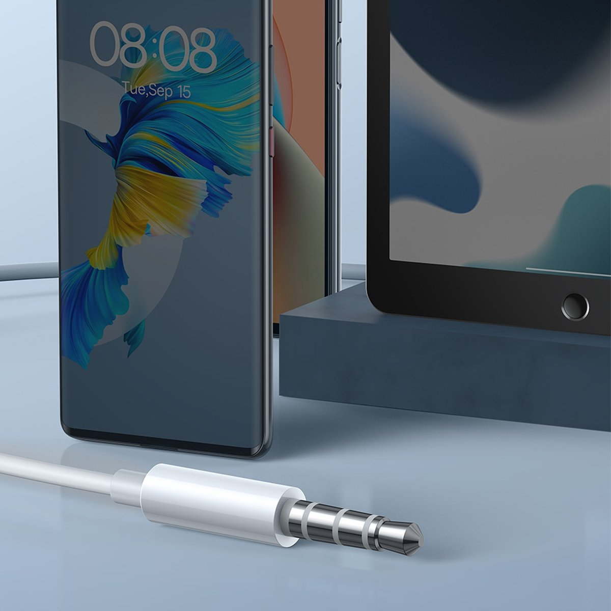 Ein weißes Audiokabel mit silbernem Ende. Es ist mit einem Telefon und einem Tablet im Hintergrund verbunden.