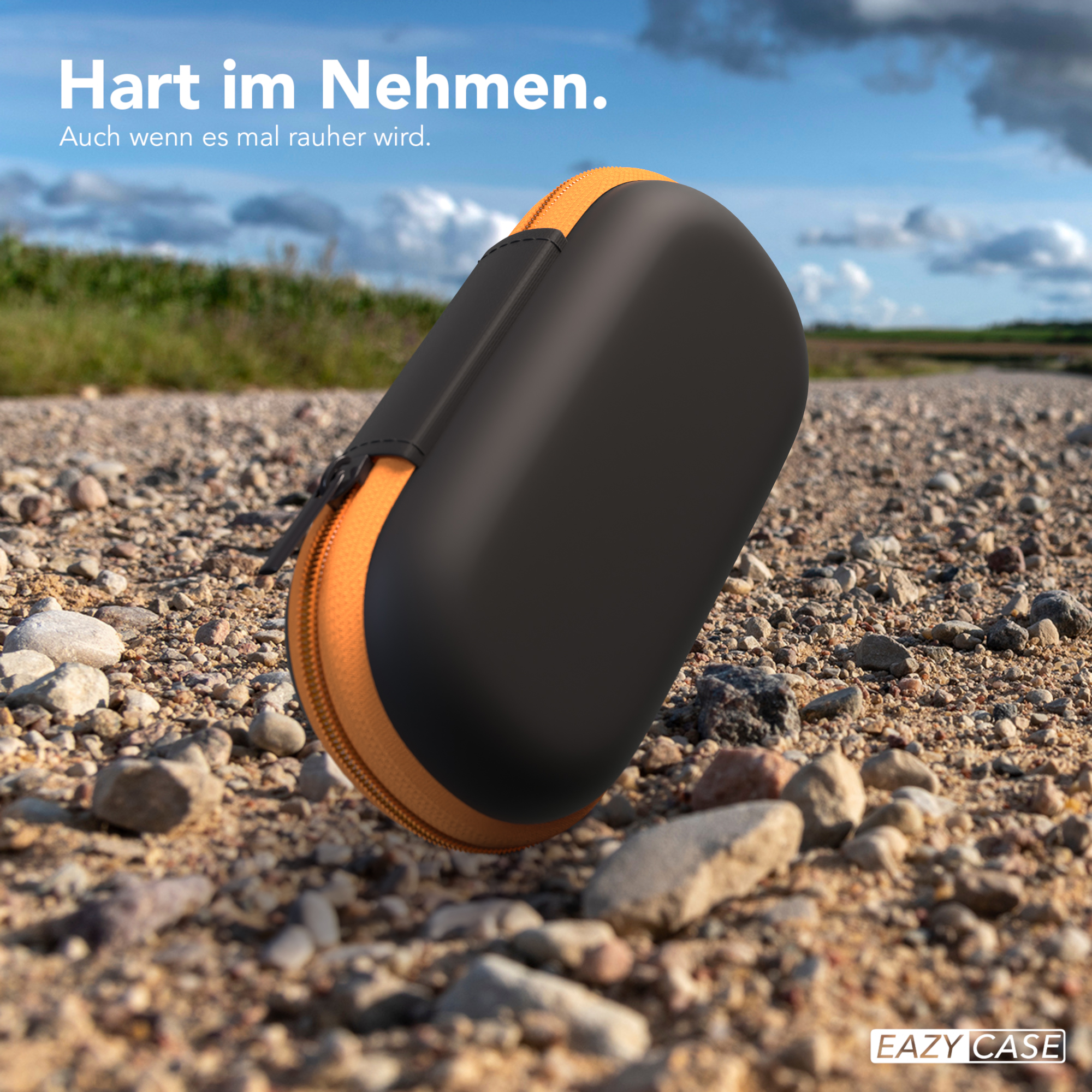 Eine schwarz-orangefarbene Hülle liegt auf einem Schotterweg. Der Text lautet "Hart im Nehmen".
