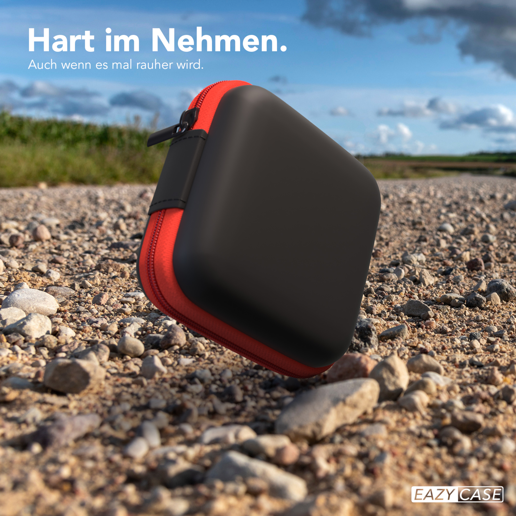 Ein schwarzes und rotes quadratisches Etui auf einem Kiesweg mit blauem Himmel im Hintergrund.