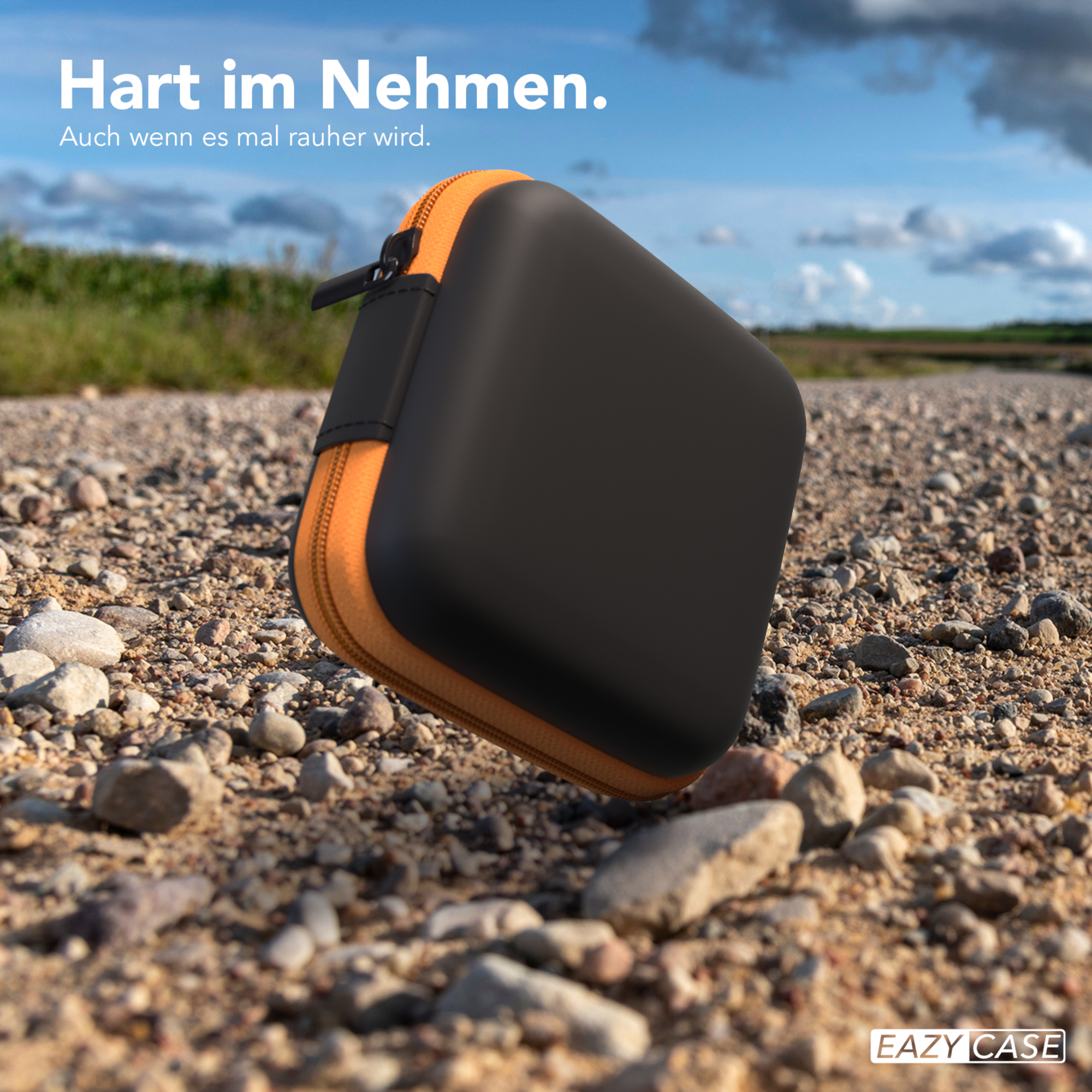 Schwarz-oranges Etui auf einem Schotterweg, mit blauem Himmel und Wolken im Hintergrund.
