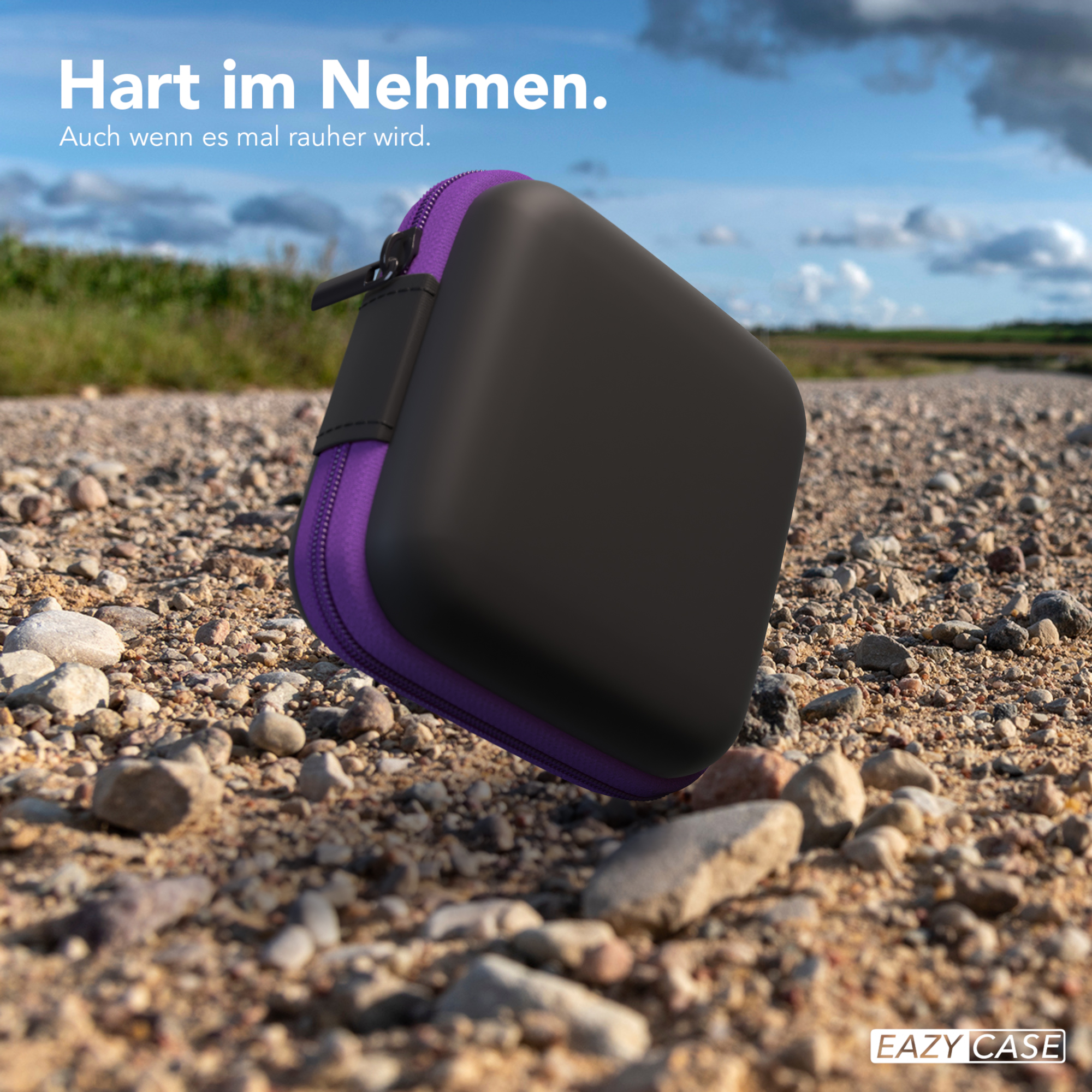 Ein schwarz-lila Reiseetui auf einem Schotterweg unter blauem Himmel.
