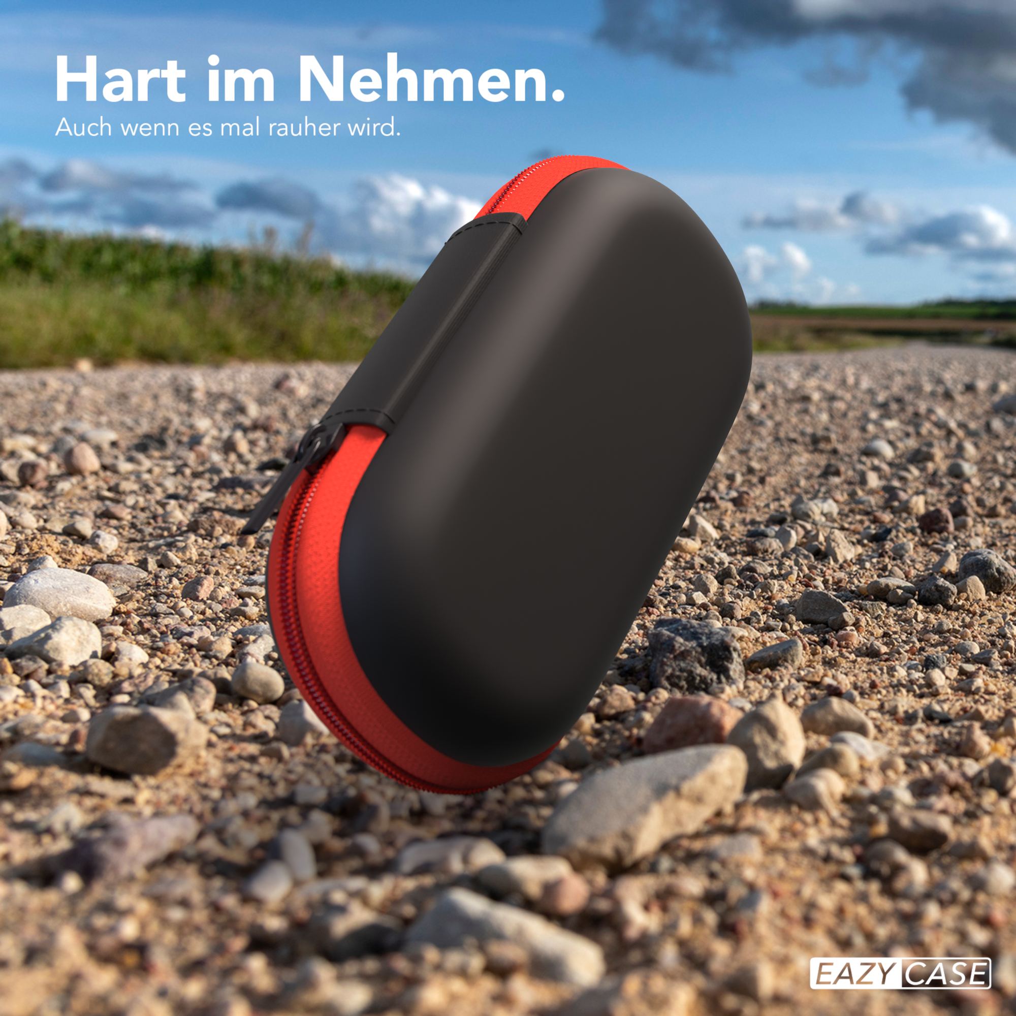 Schwarz-rotes Etui auf einem Schotterweg. Text in Deutsch. Verschwommener Naturhintergrund.