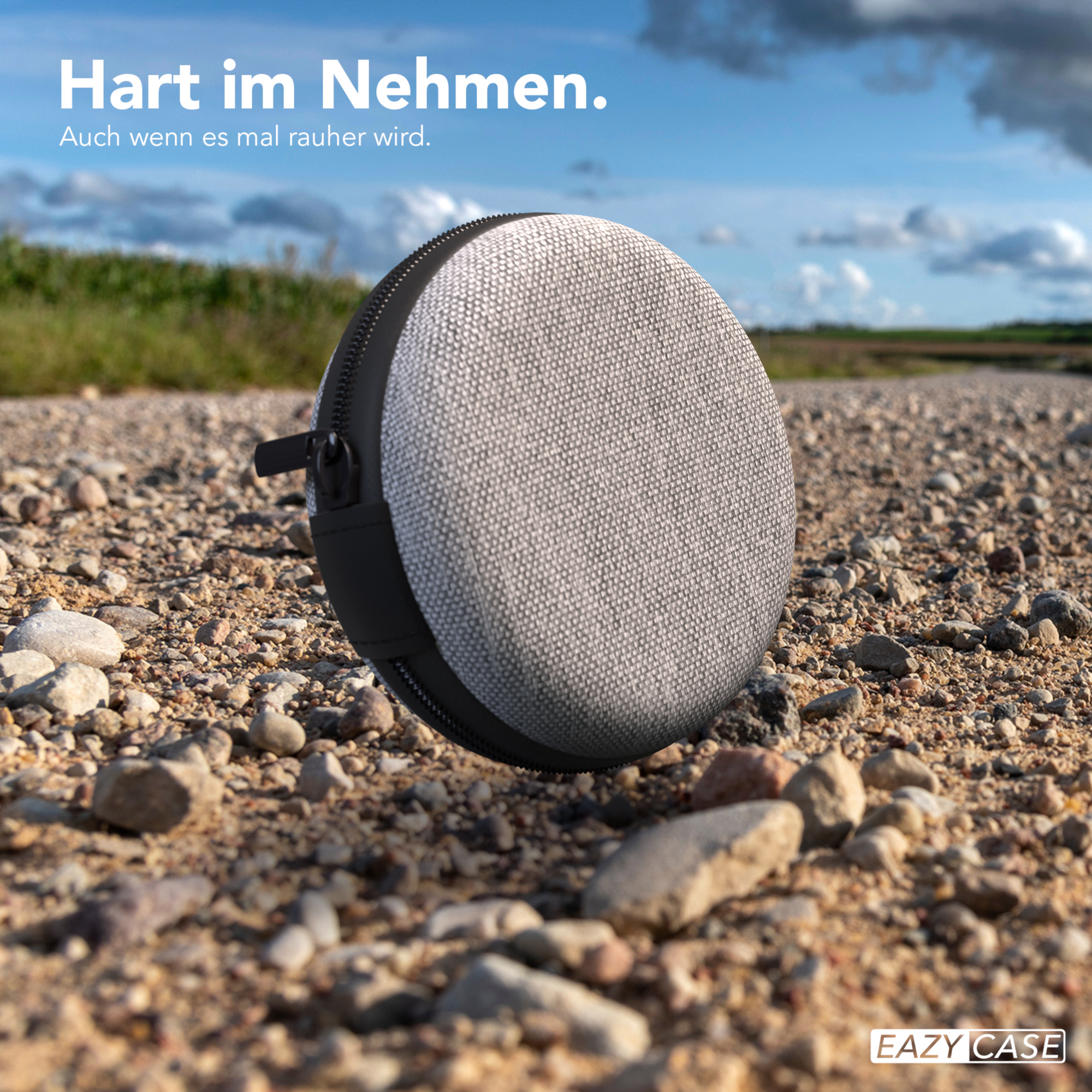 Runder, grauer Lautsprecherkoffer auf einem Schotterweg mit blauem Himmel.