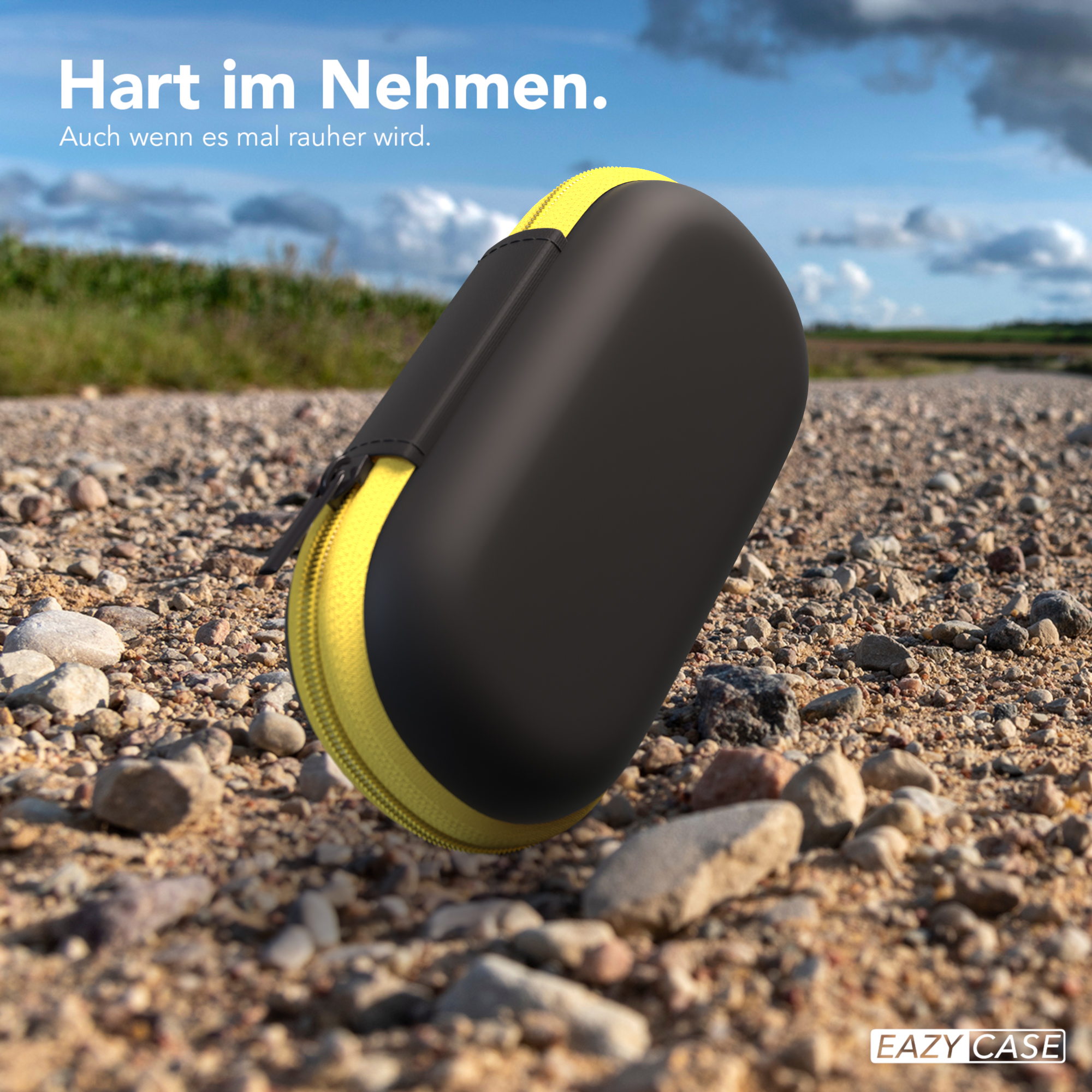 Schwarz-gelbes Etui auf einem Schotterweg. Das Etui ist geschlossen und der Reißverschluss ist sichtbar.